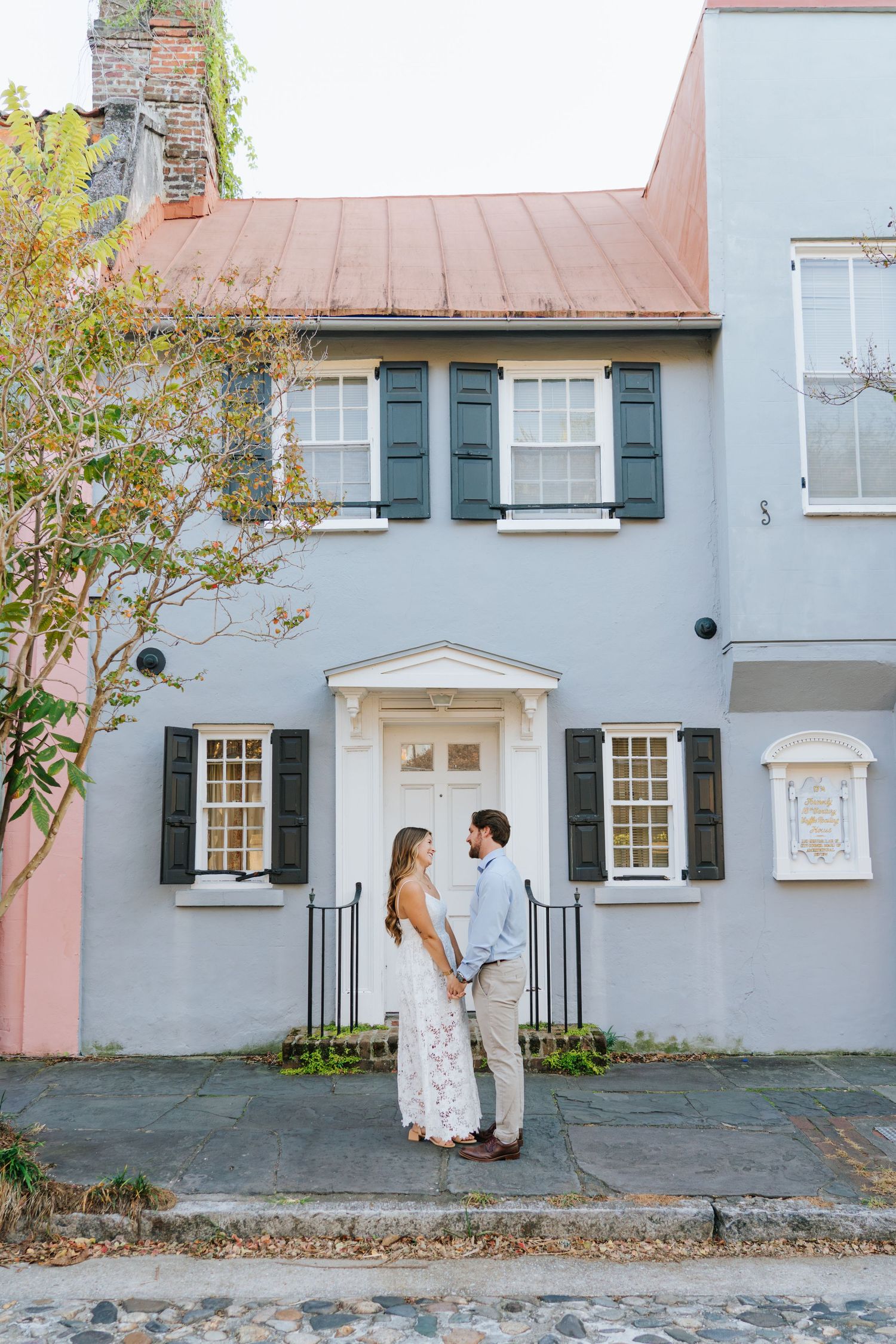 A couple shares intimate moments against a charming pastel-colored building exterior.