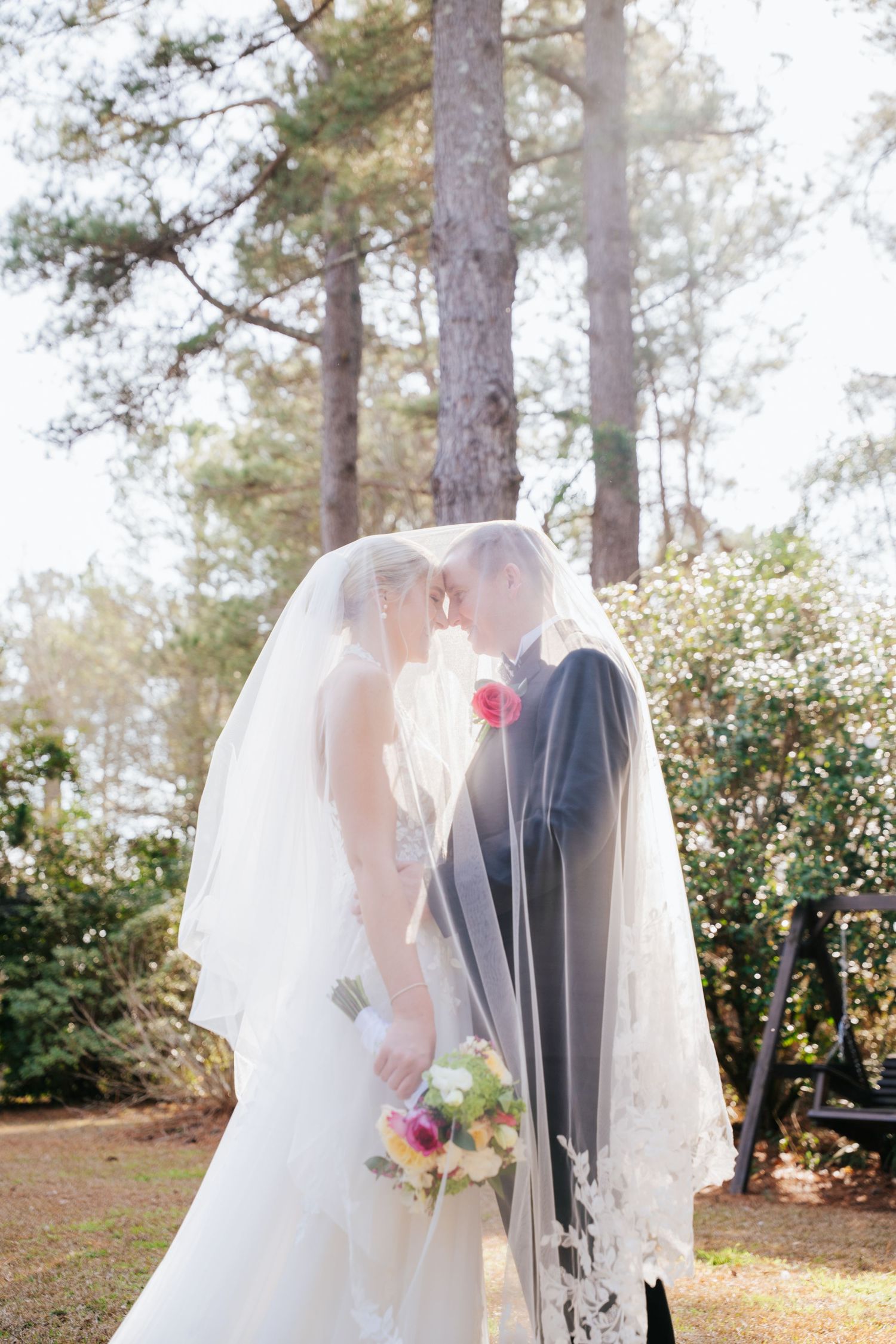 Romantic outdoor wedding scene with bride and groom sharing intimate moments among pine trees and sunlit foliage.
