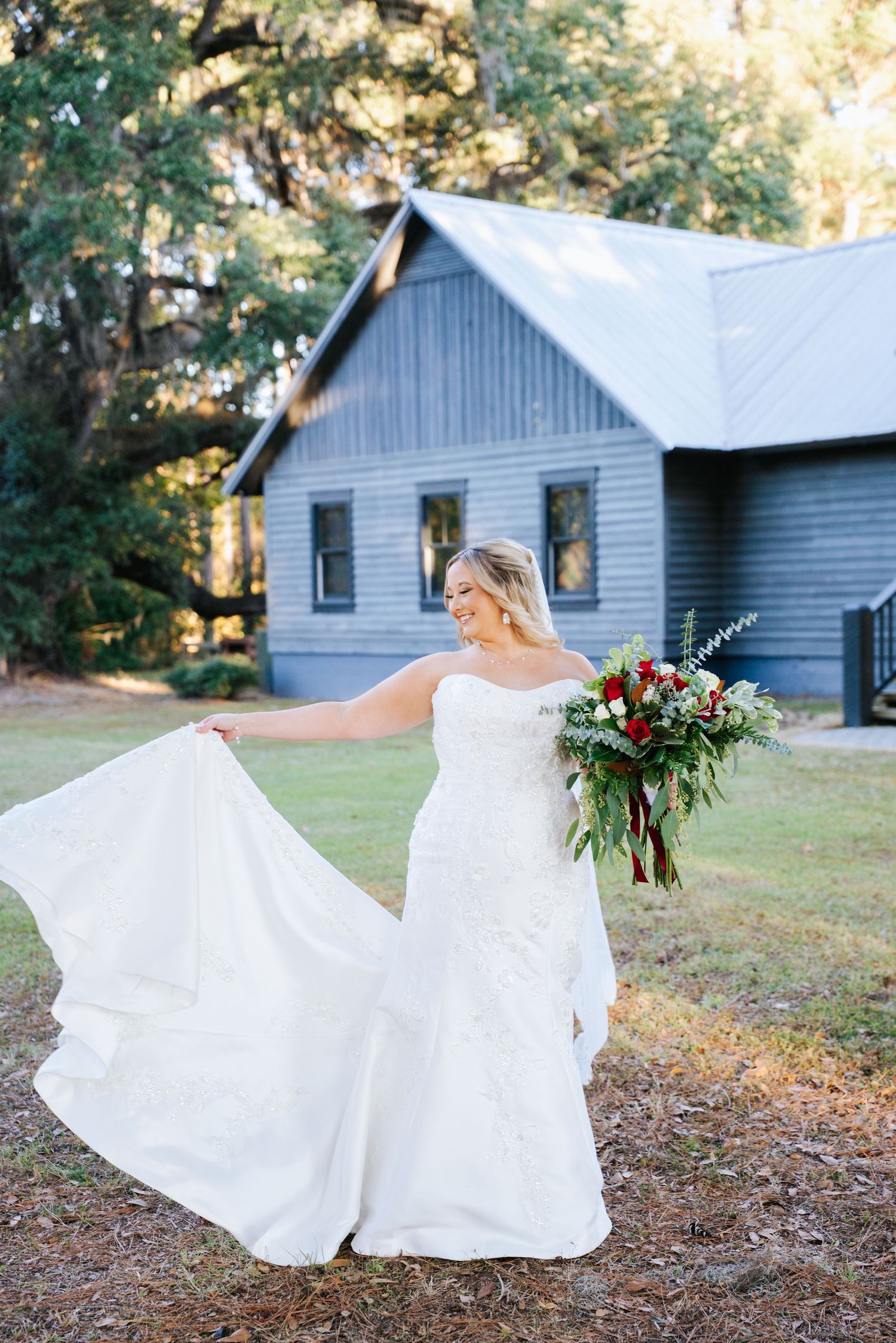 A flowing white wedding dress twirls against a rustic blue chapel backdrop as a bouquet of red flowers is held aloft.