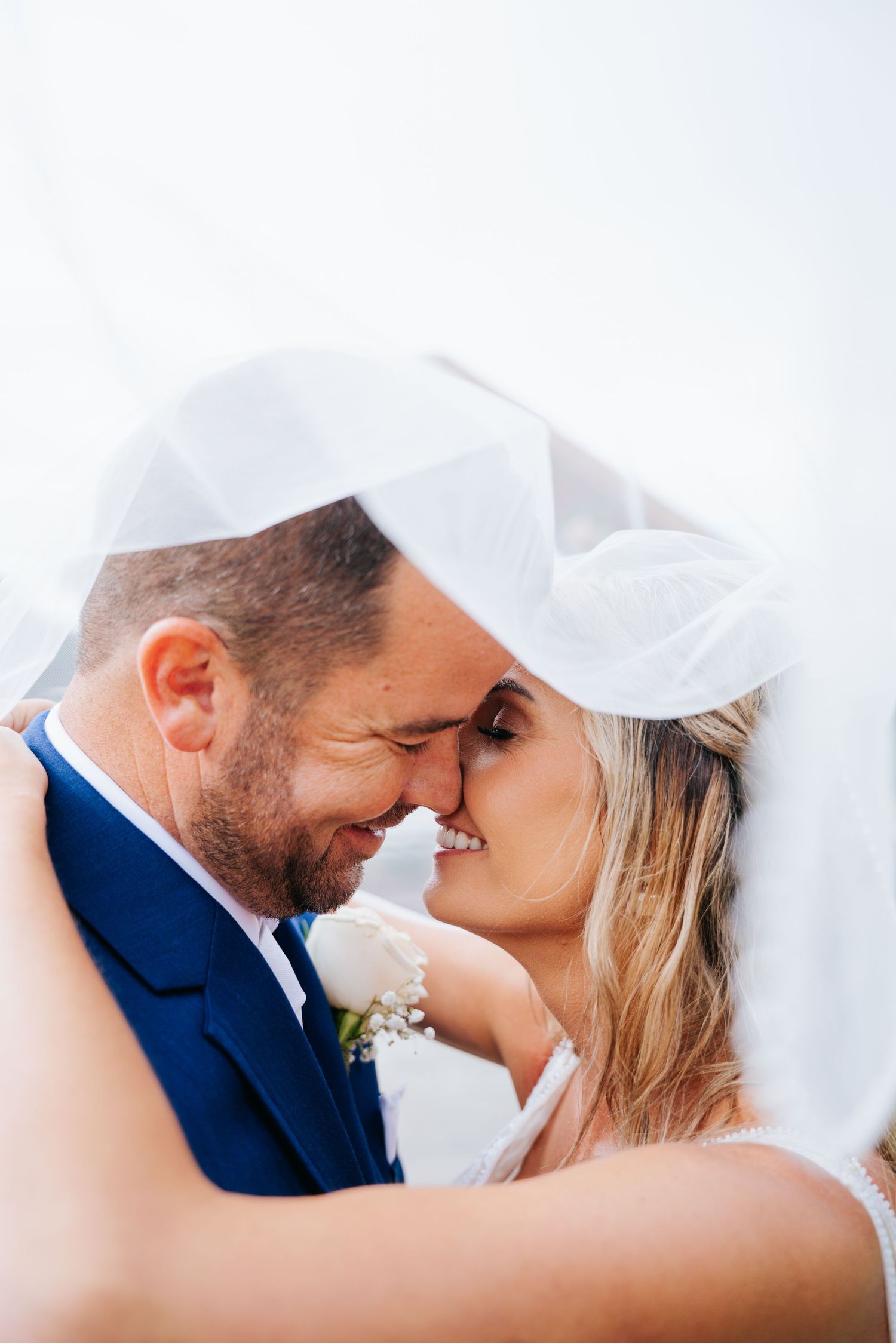 Intimate moment shared under flowing white veil during wedding photoshoot.