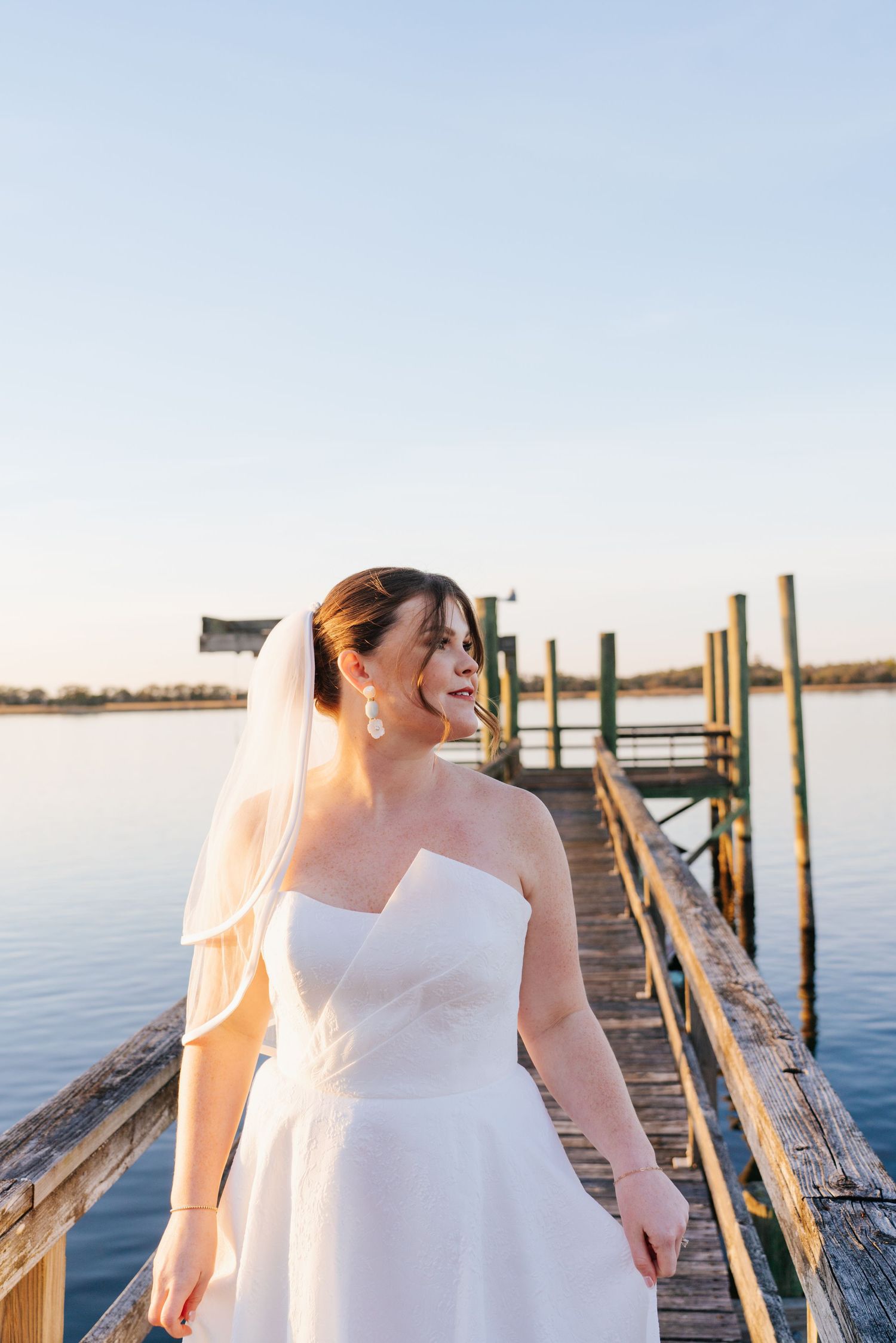 Wedding photography on a wooden dock overlooking calm waters during golden hour.