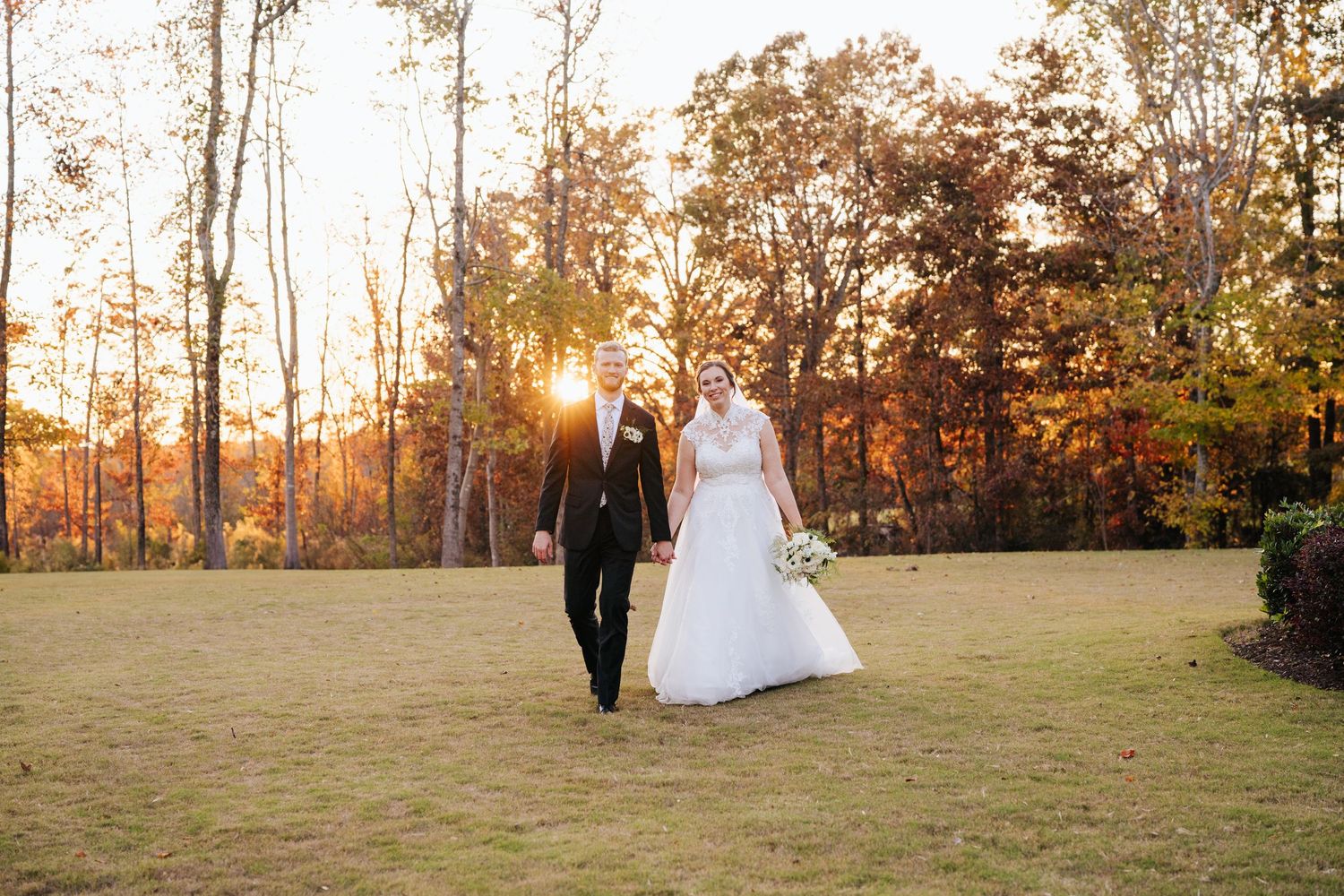 Silhouetted couple walks through autumn field at sunset after their wedding ceremony.