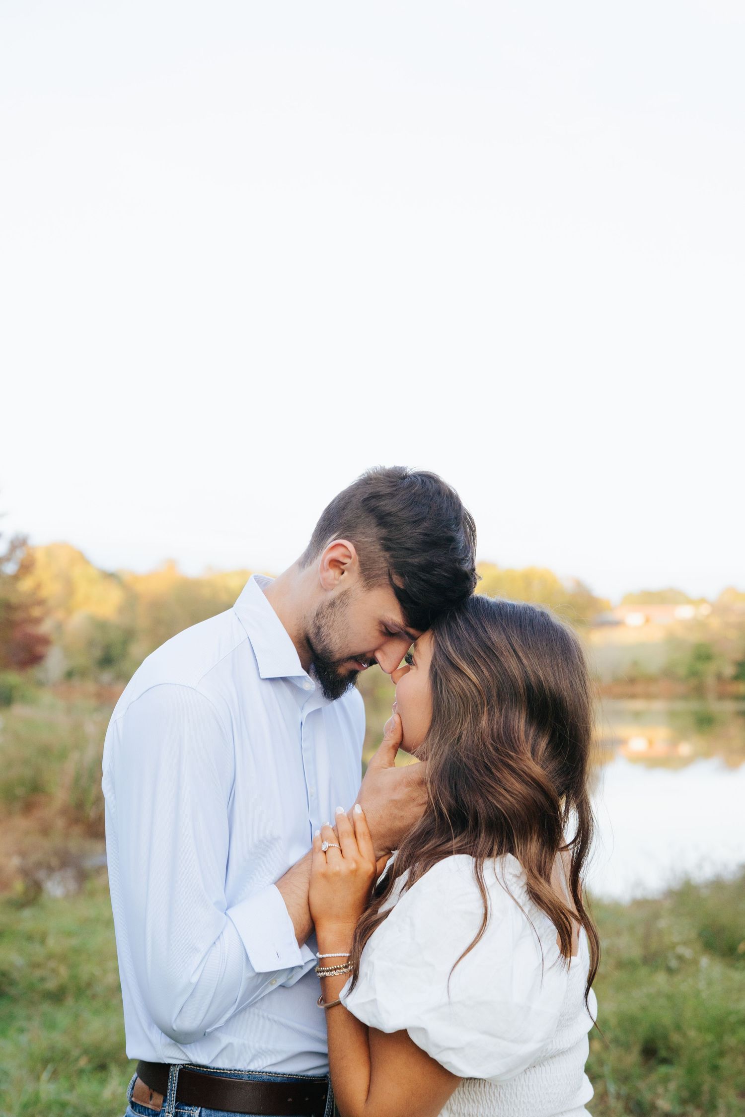 A romantic couple shares tender kisses in a natural outdoor setting with golden sunlight and greenery.