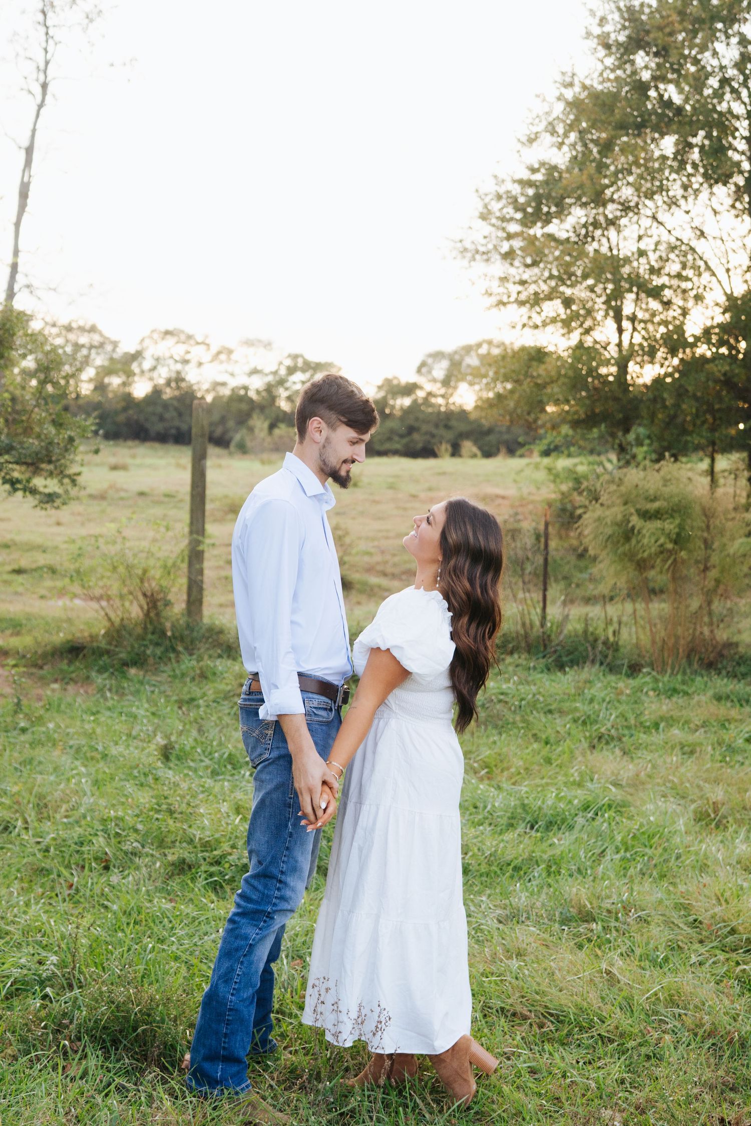 A couple in casual white outfits share a romantic moment in a sunlit meadow during golden hour.