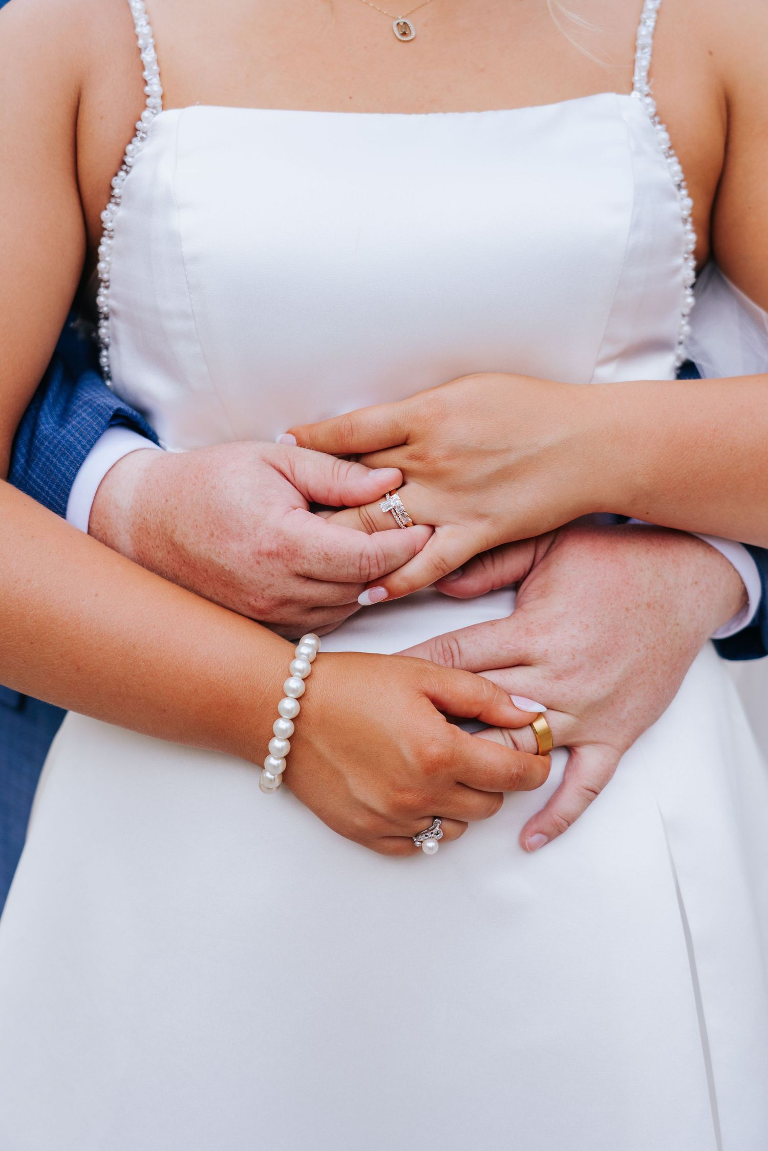 Close-up of hands wearing pearl bracelet and engagement ring against white dress.