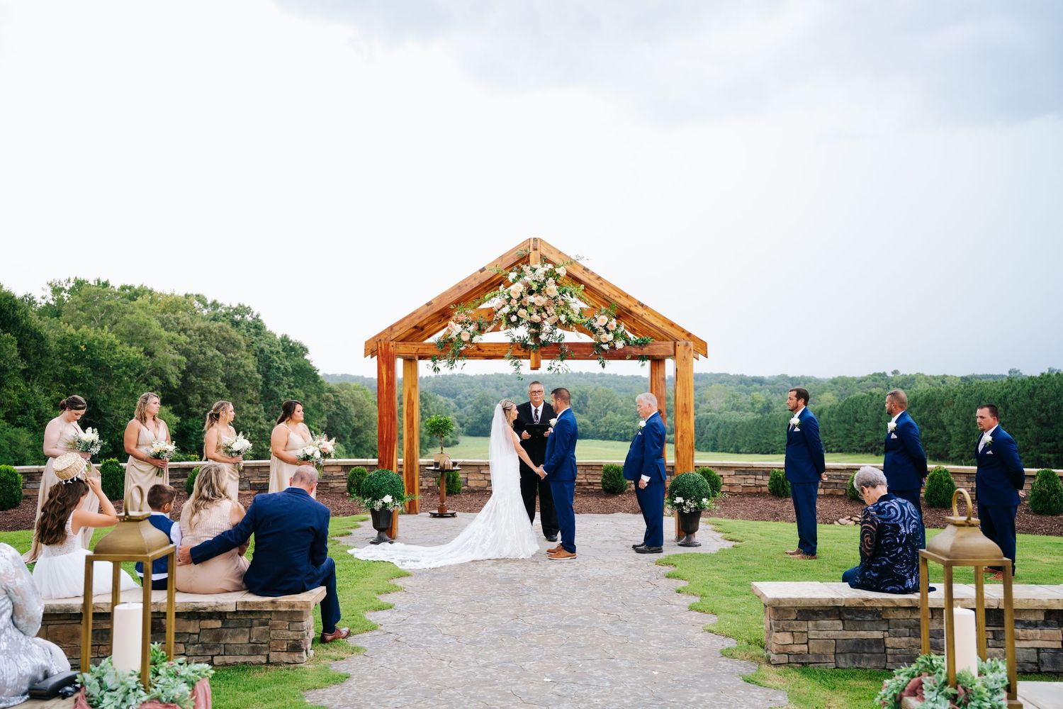 Wedding ceremony under wooden gazebo with wedding party in attendance.