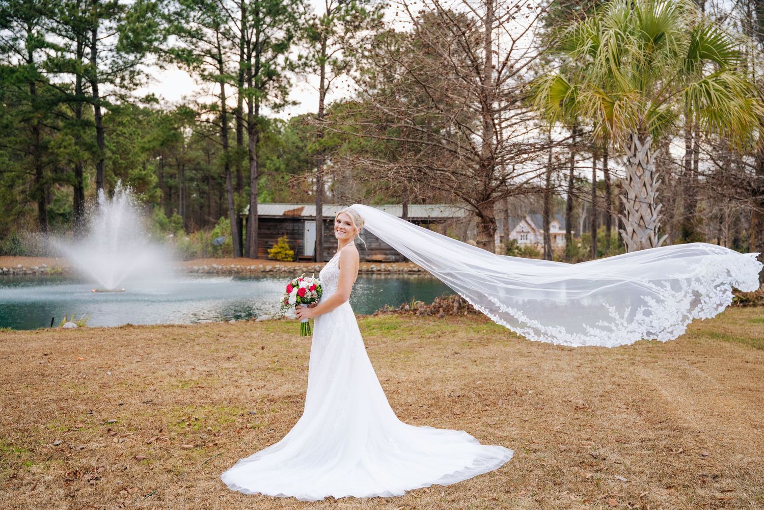 A flowing white wedding dress billows dramatically in the wind against a natural outdoor backdrop.