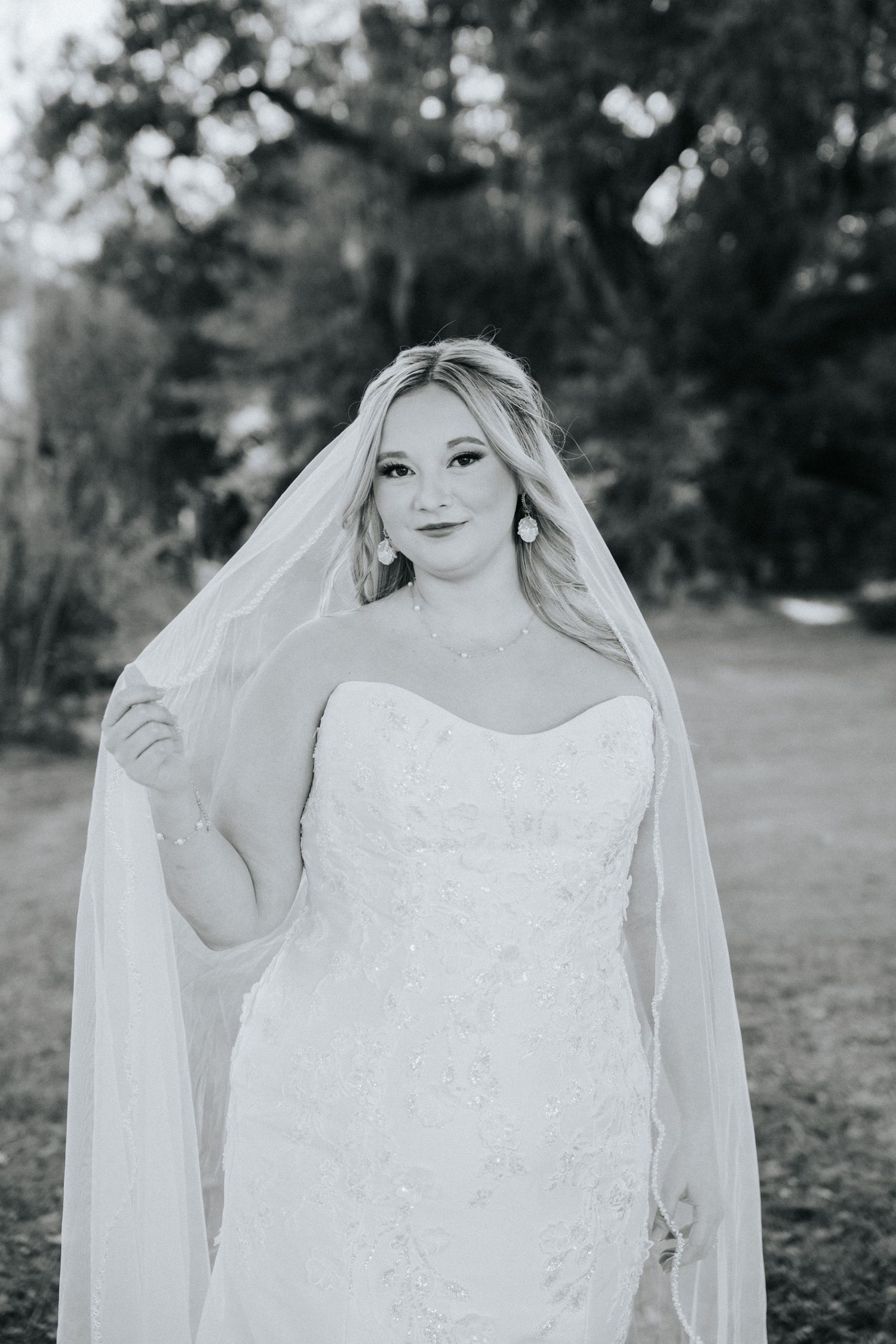 Black and white bridal portrait featuring a bride in a strapless lace gown with flowing veil in an outdoor setting.