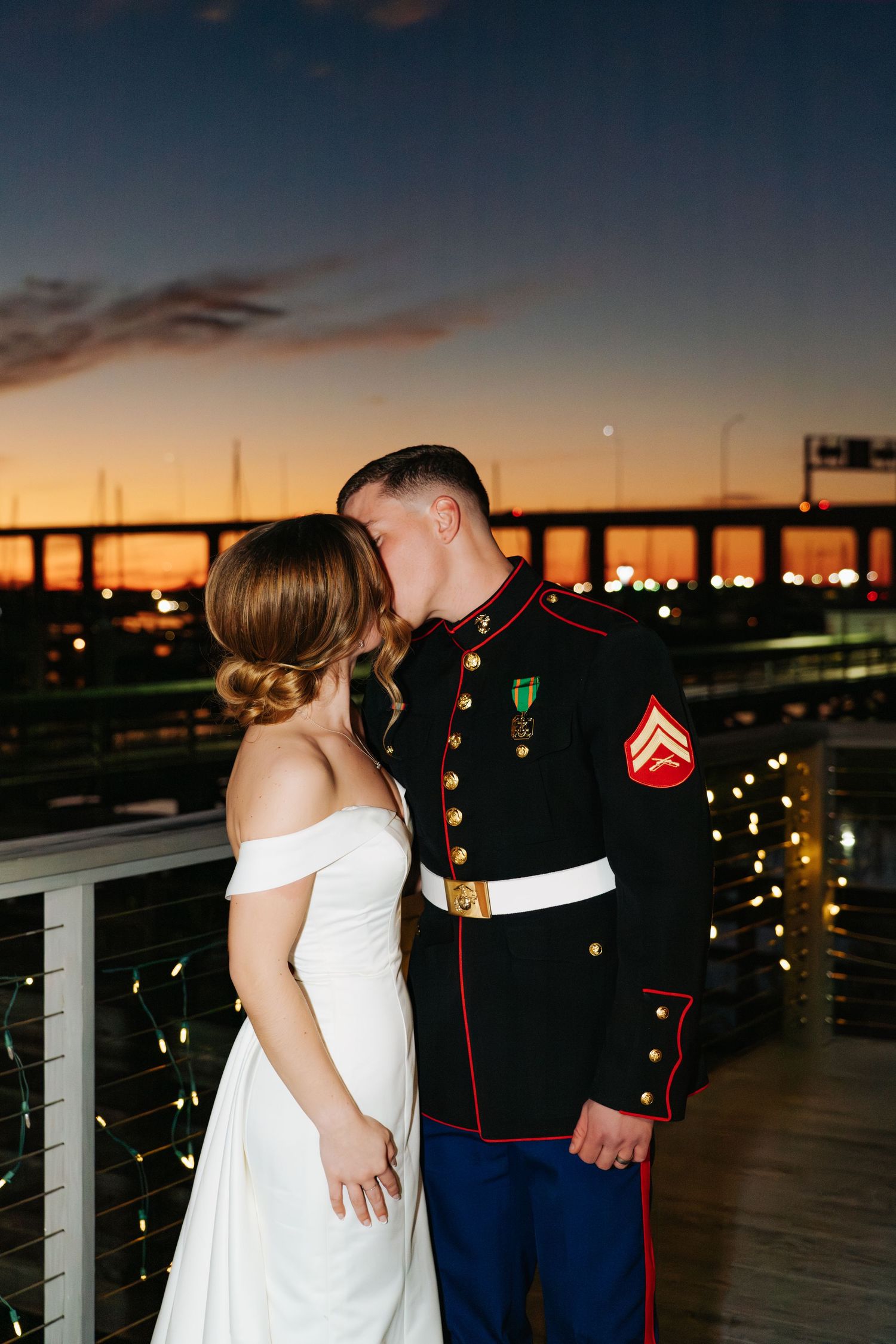 A romantic sunset wedding portrait on a deck with city lights in the background.
