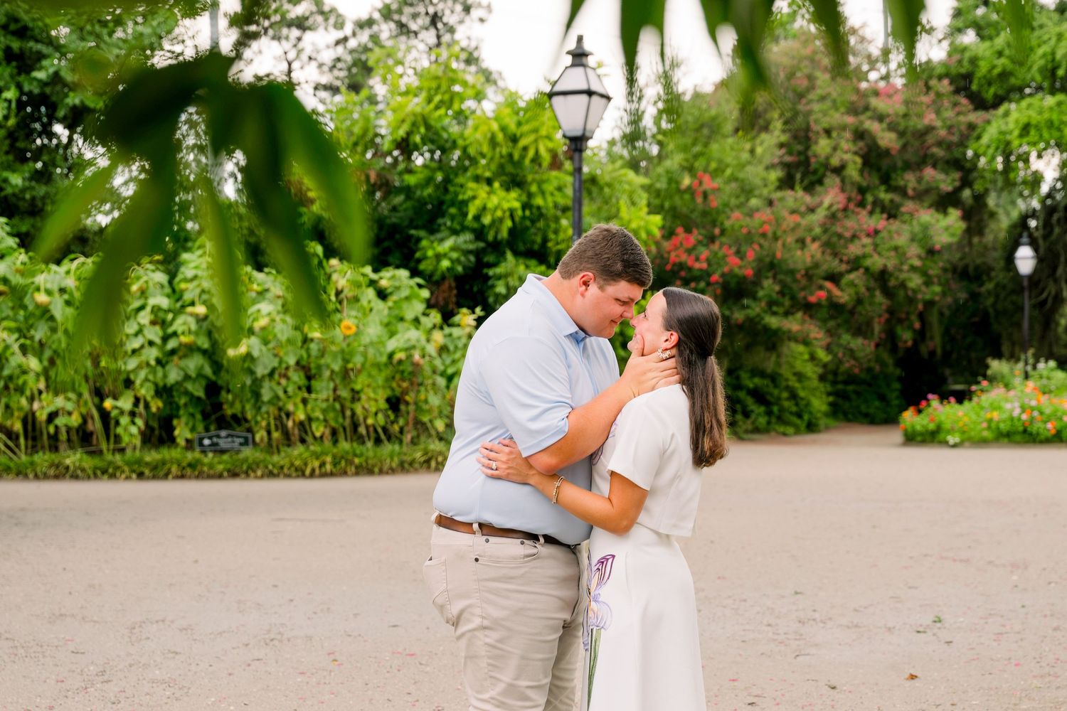 Couple sharing a romantic moment in a lush green park, man in blue shirt leaning toward woman in white dress.
