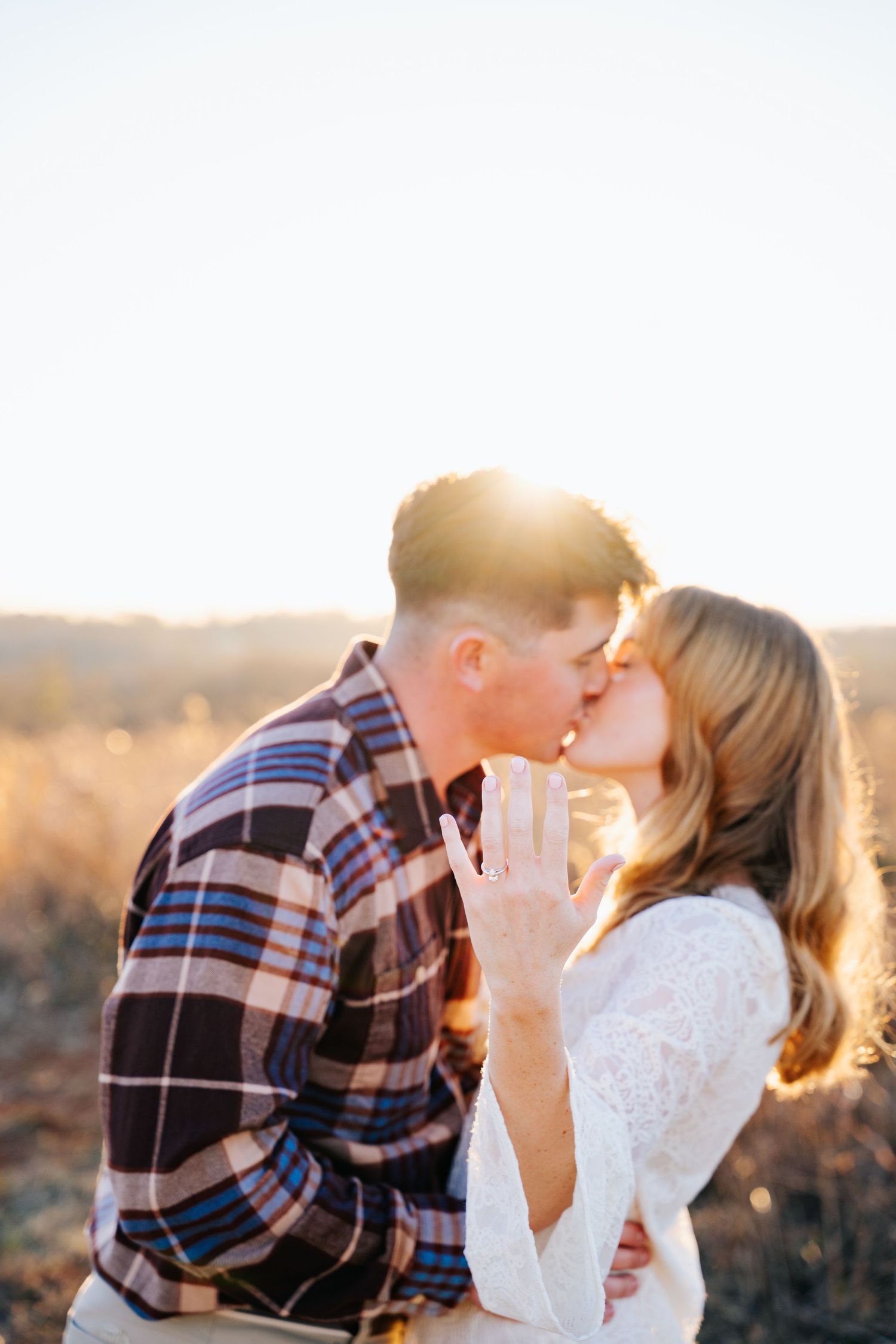 A couple shares an intimate moment at sunset in a plaid shirt and white lace dress.