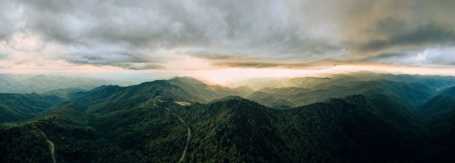 Panoramic mountain landscape view at sunset with dramatic cloudy skies.