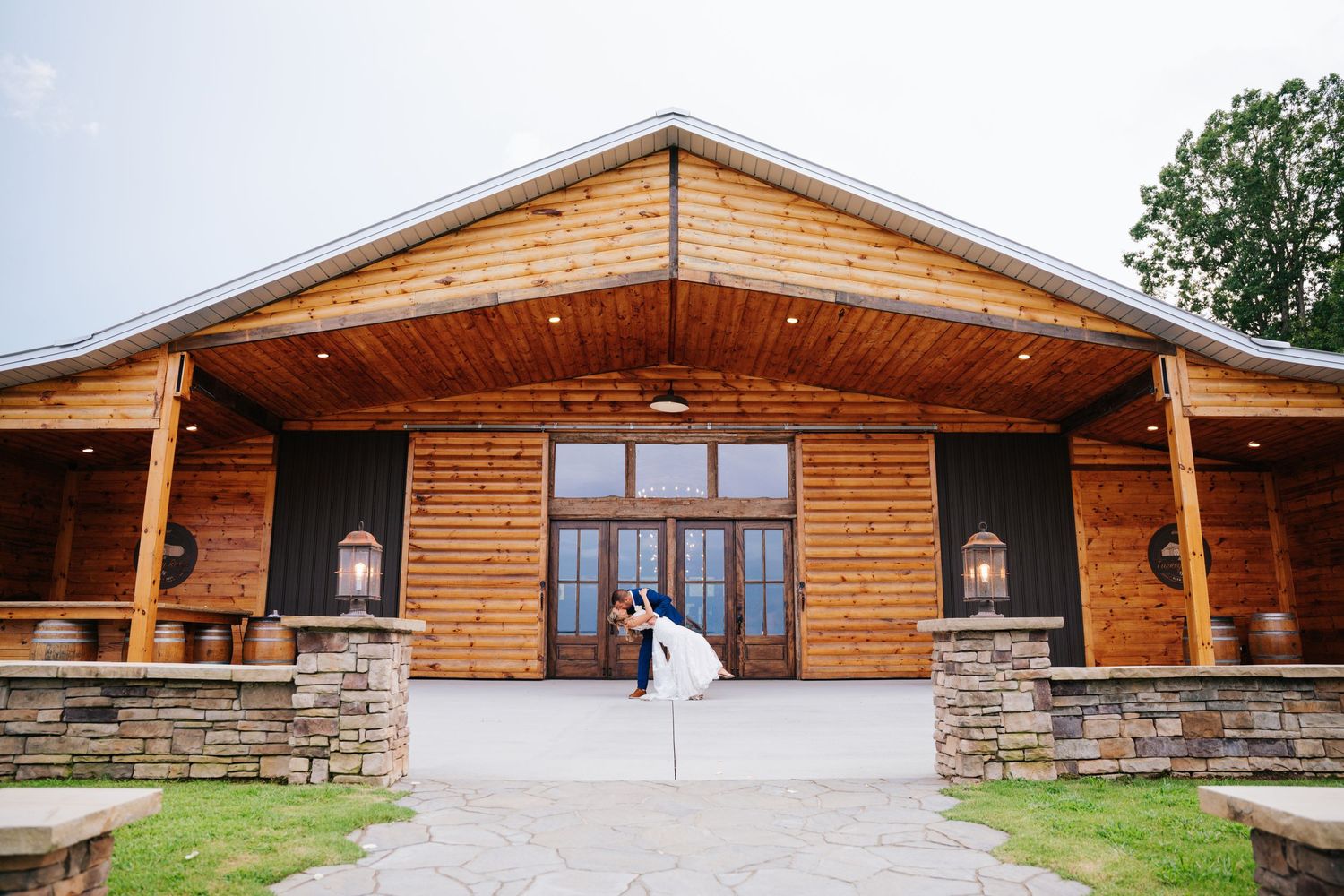 A rustic wooden wedding venue with stone pillars and large windows stretches across the landscape.
