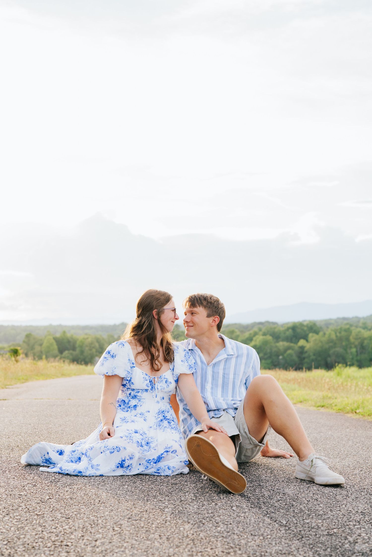 A couple in coordinating blue and white outfits share romantic moments while sitting on a country road.
