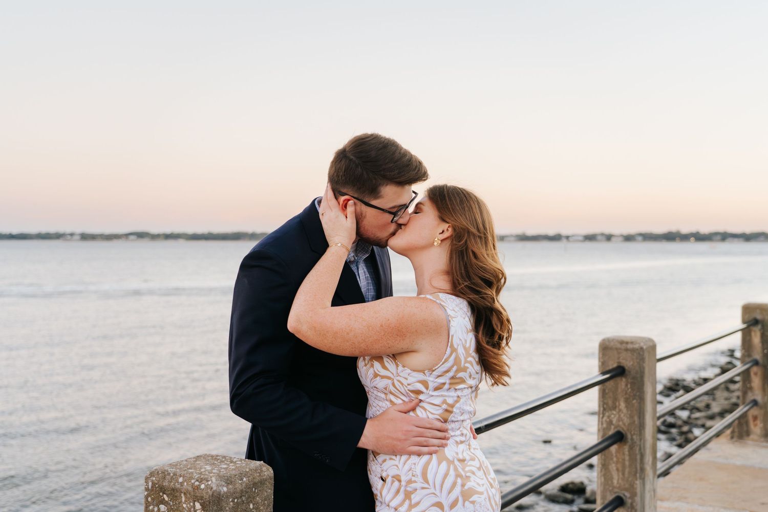 A romantic waterfront moment at sunset with the couple sharing a kiss.