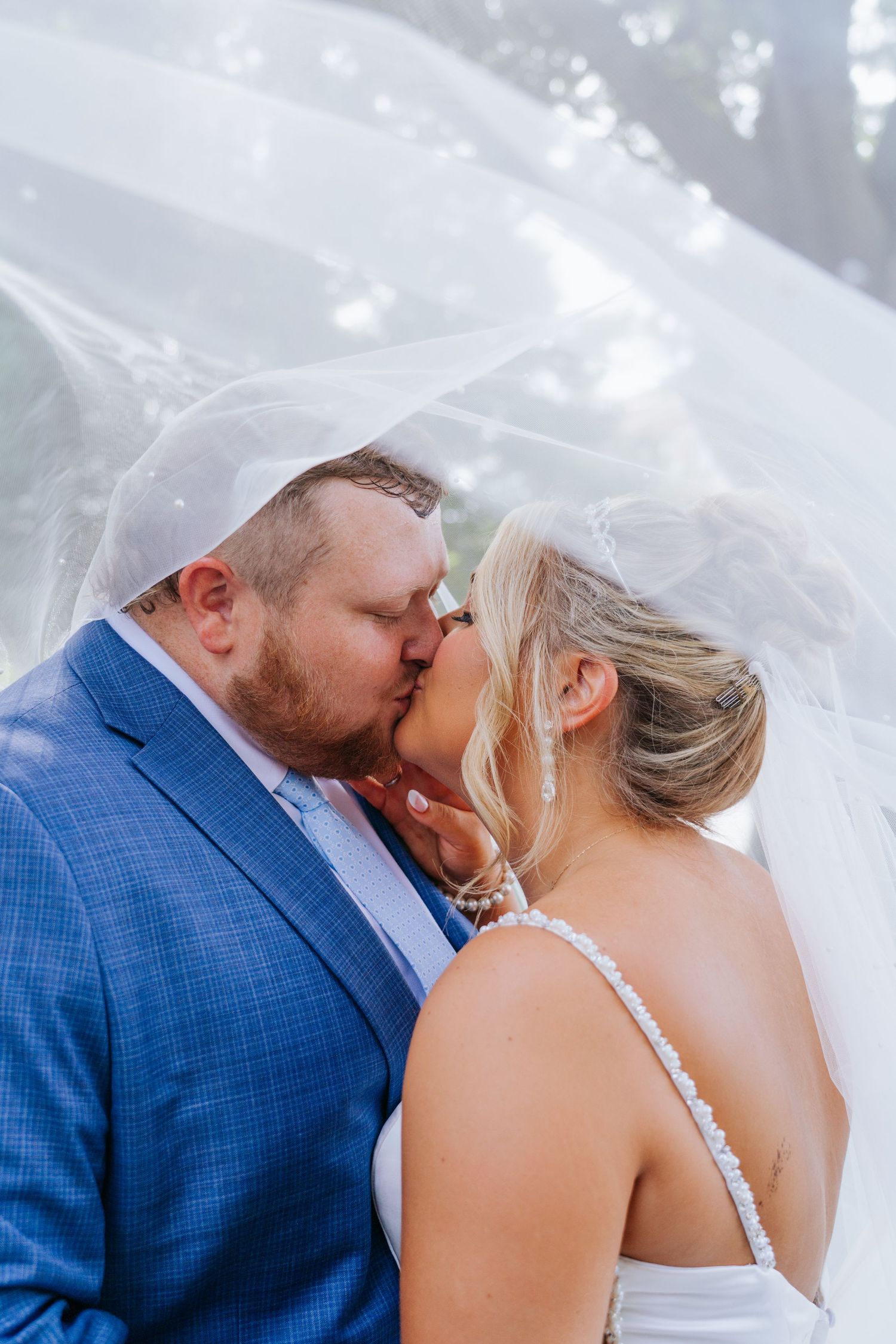 Close-up wedding photos of a tender kiss under a flowing white veil.
