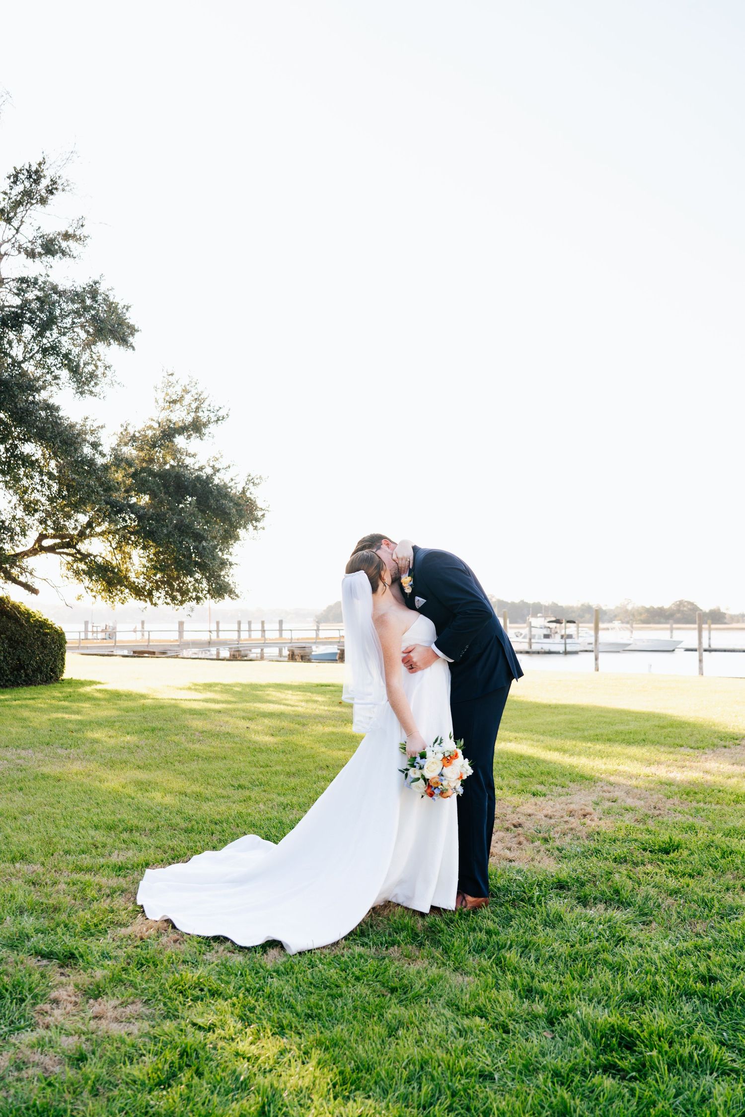 Romantic wedding photos taken on a grassy hill overlooking the water at sunset.