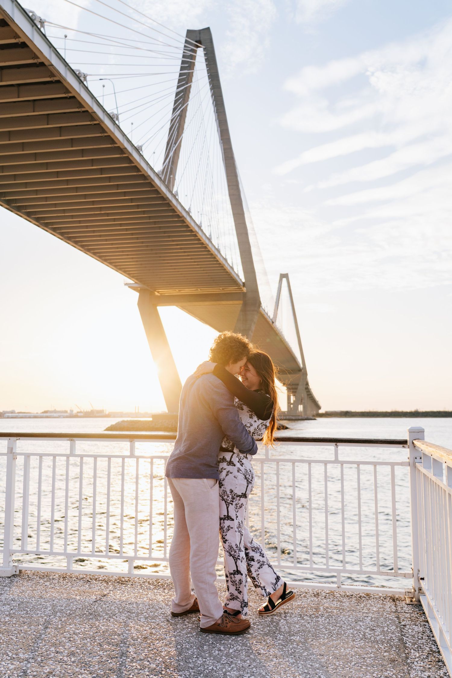 Couple sharing a romantic moment at sunset beneath the Ravenel Bridge.