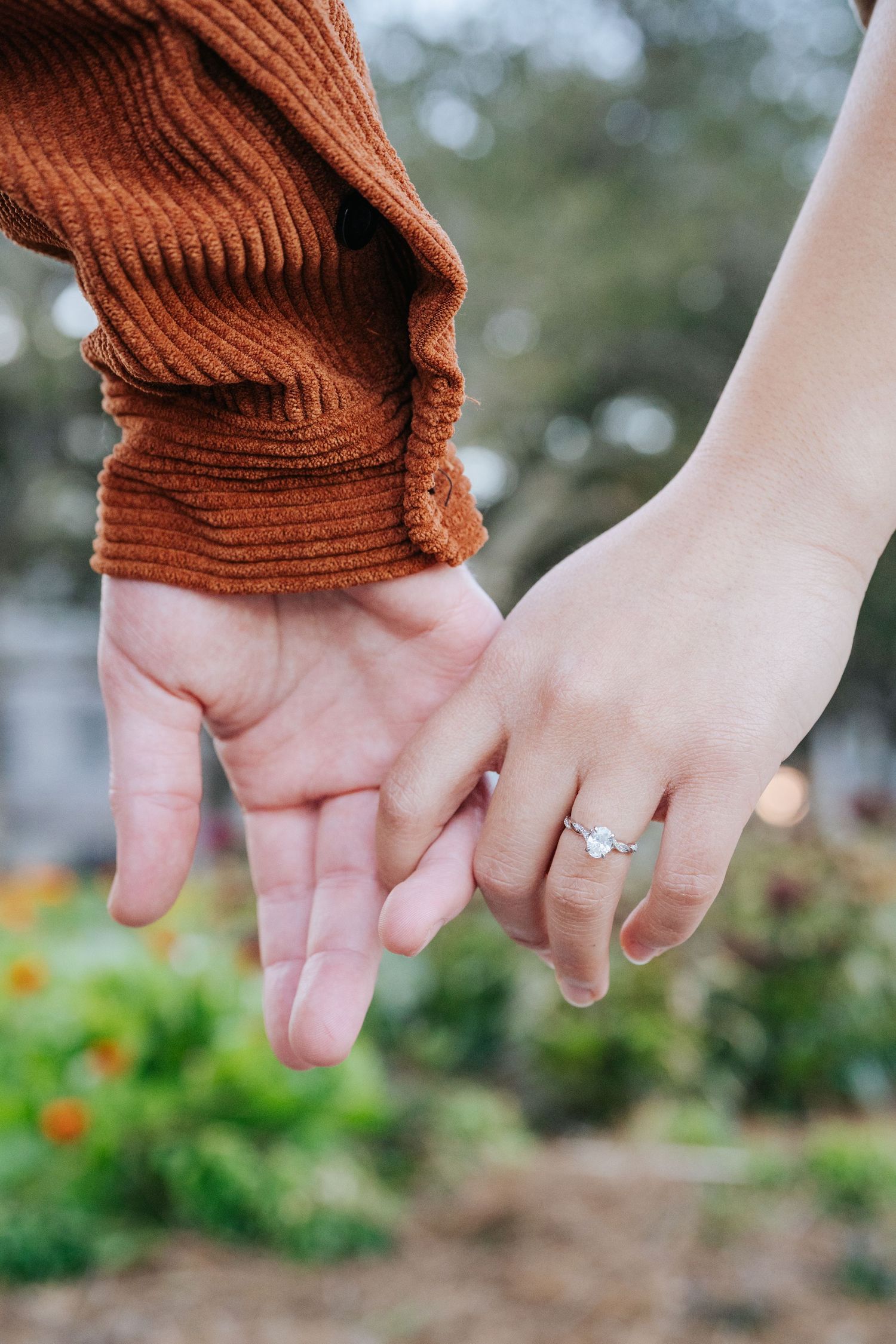 Close-up of hands showing off engagement ring against garden background.