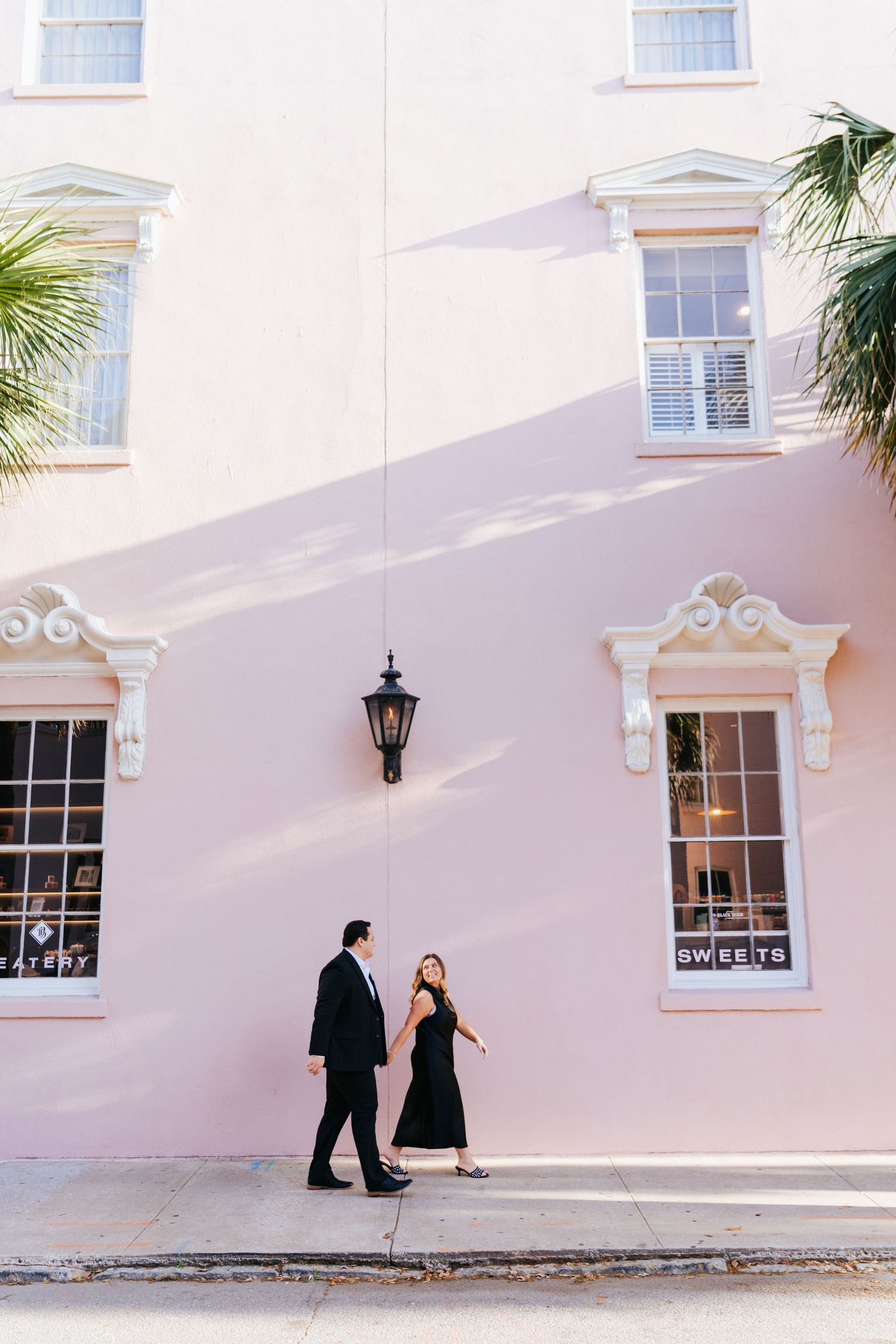 A couple poses dramatically against a pink building with classic Charleston architecture.
