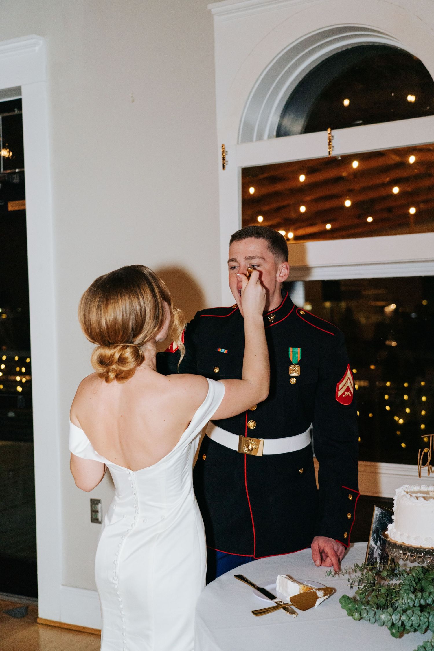 Wedding reception scene showing cake cutting moment in an elegant white-walled venue.