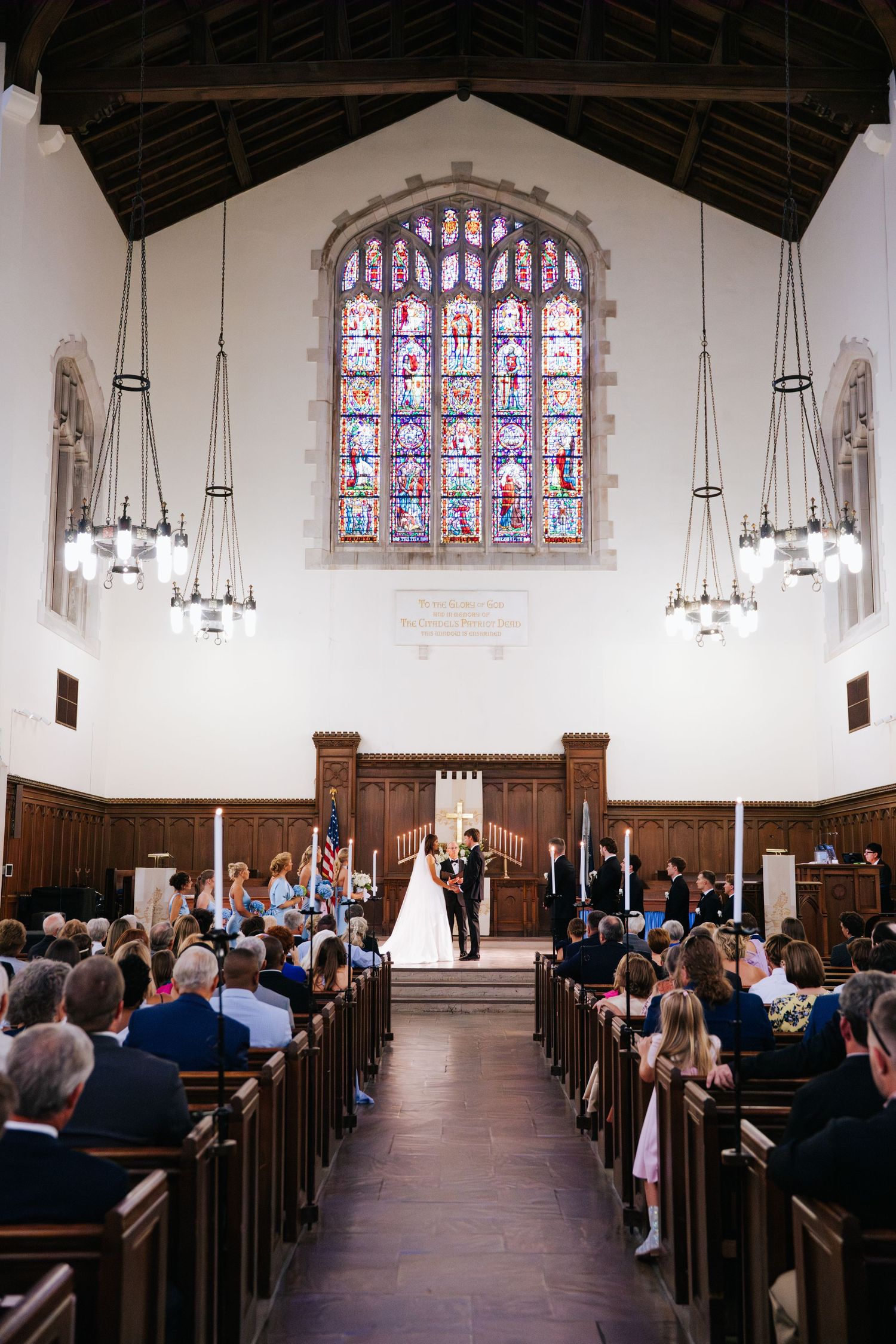 Wide angle view of a wedding ceremony in the Citadel chapel with vaulted ceilings and stained glass.