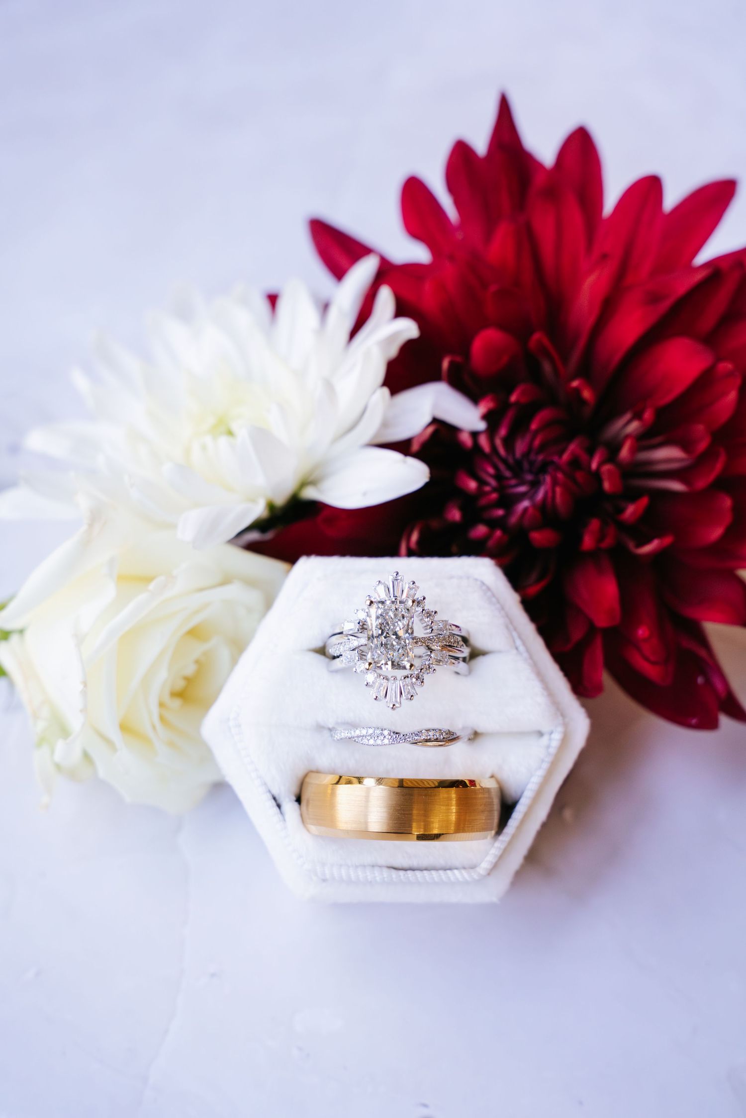Wedding rings displayed on white hexagonal ring holders with red and white dahlias in a minimalist photo series.