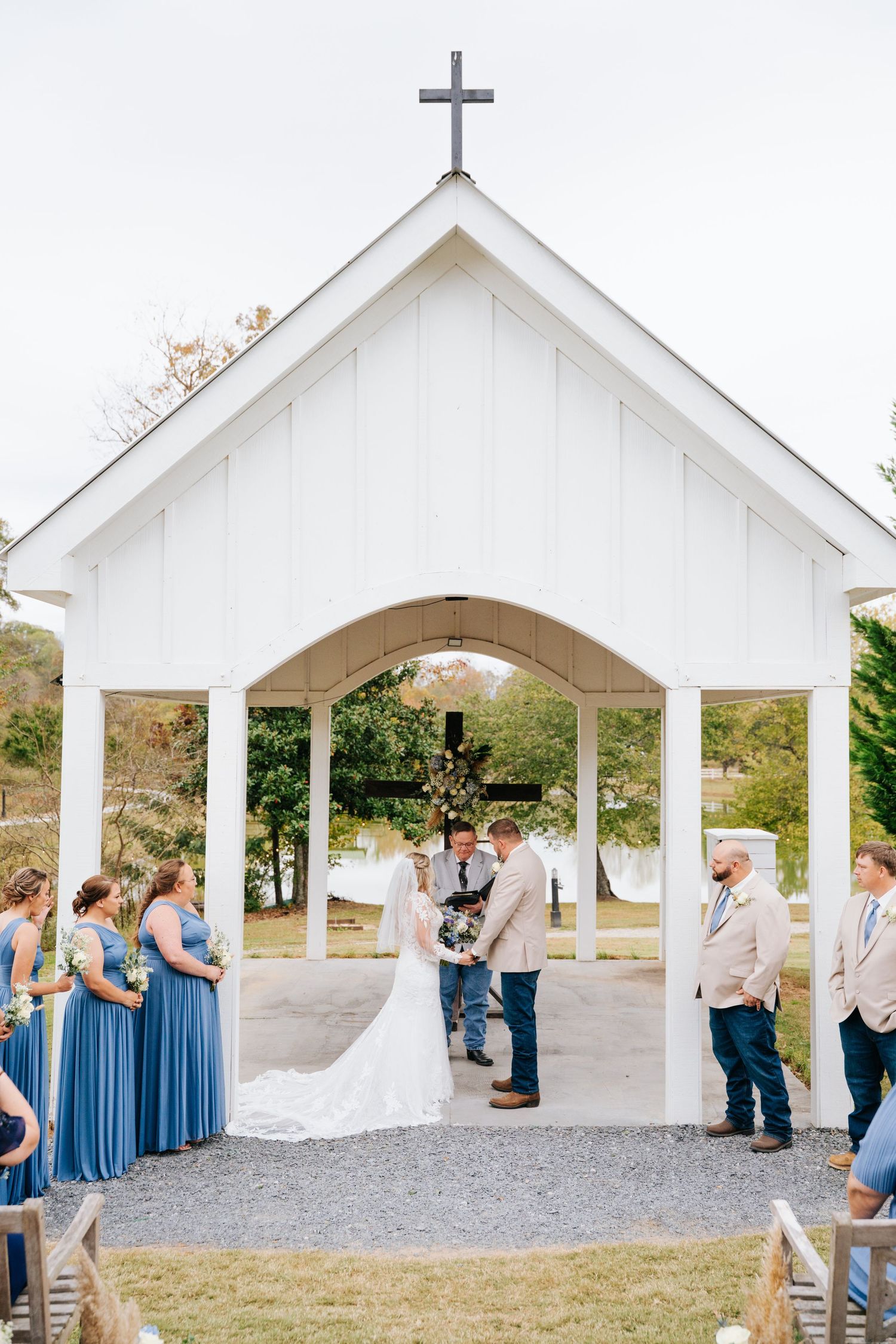Wedding ceremony taking place under a white chapel gazebo with blue-dressed bridesmaids and groomsmen in attendance.