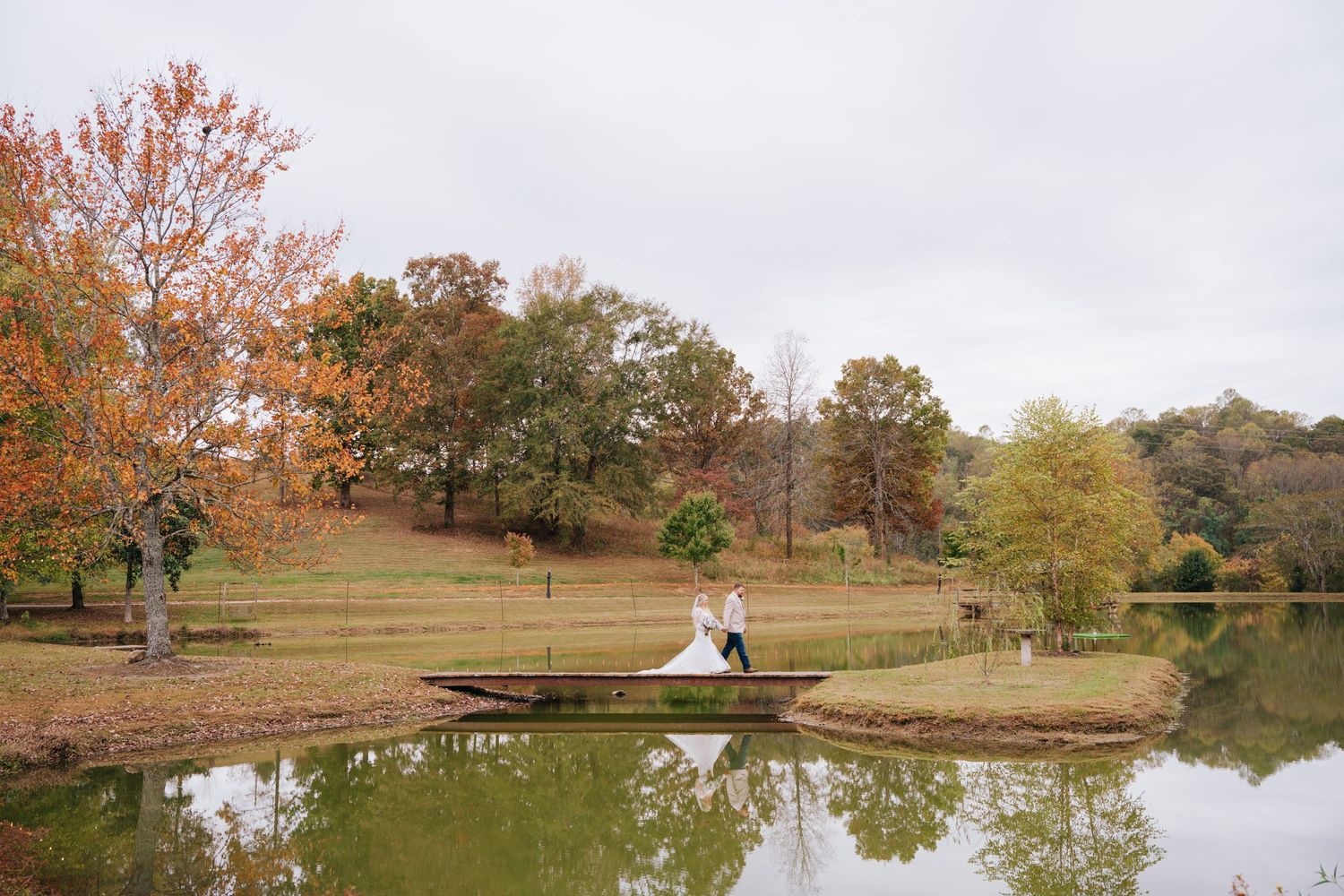 Scenic autumn landscape with trees reflecting in a tranquil pond and a rustic wooden bridge in the park.