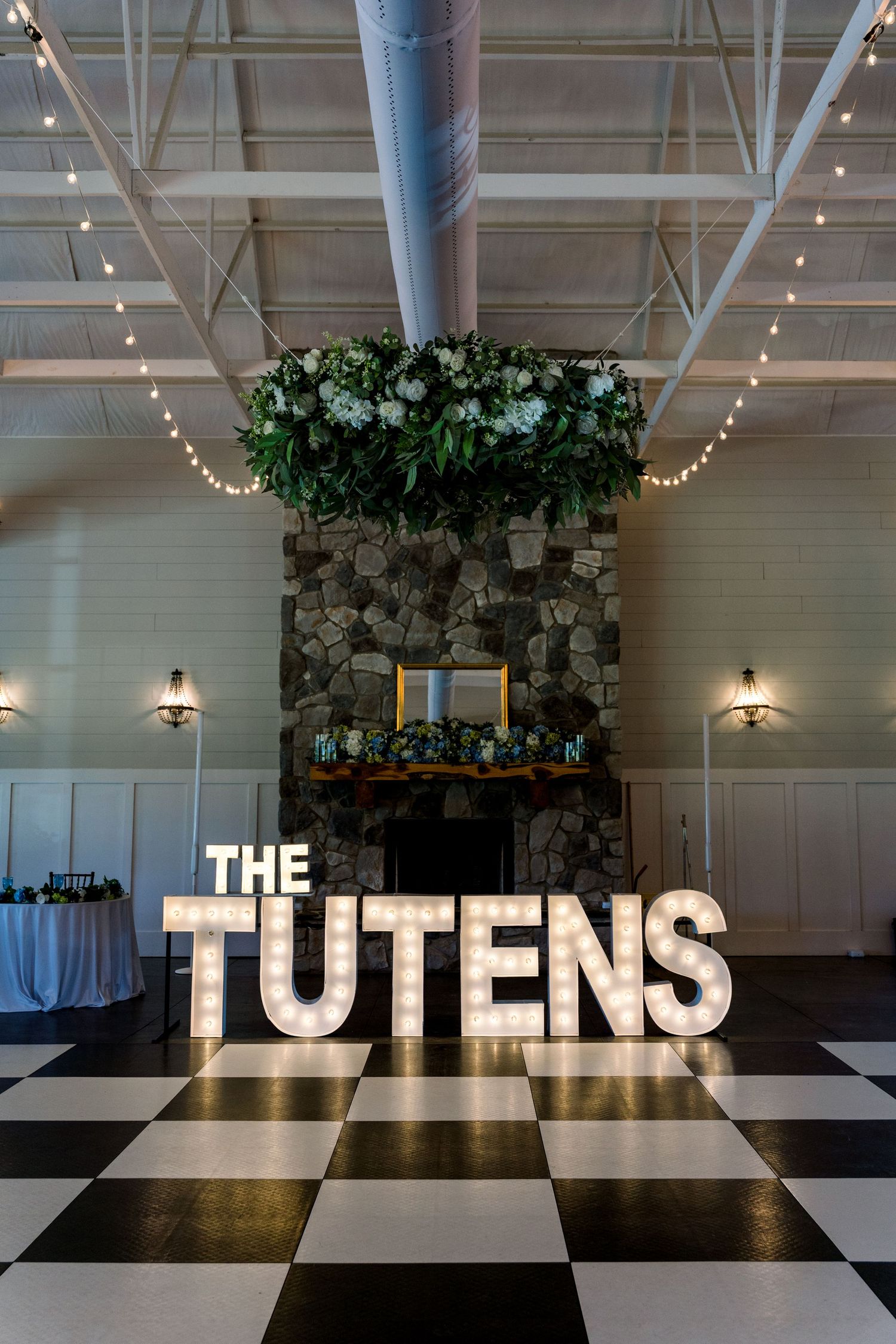 Illuminated marquee letters spelling THE TUTENS on a black and white checkered dance floor at an elegant wedding reception.