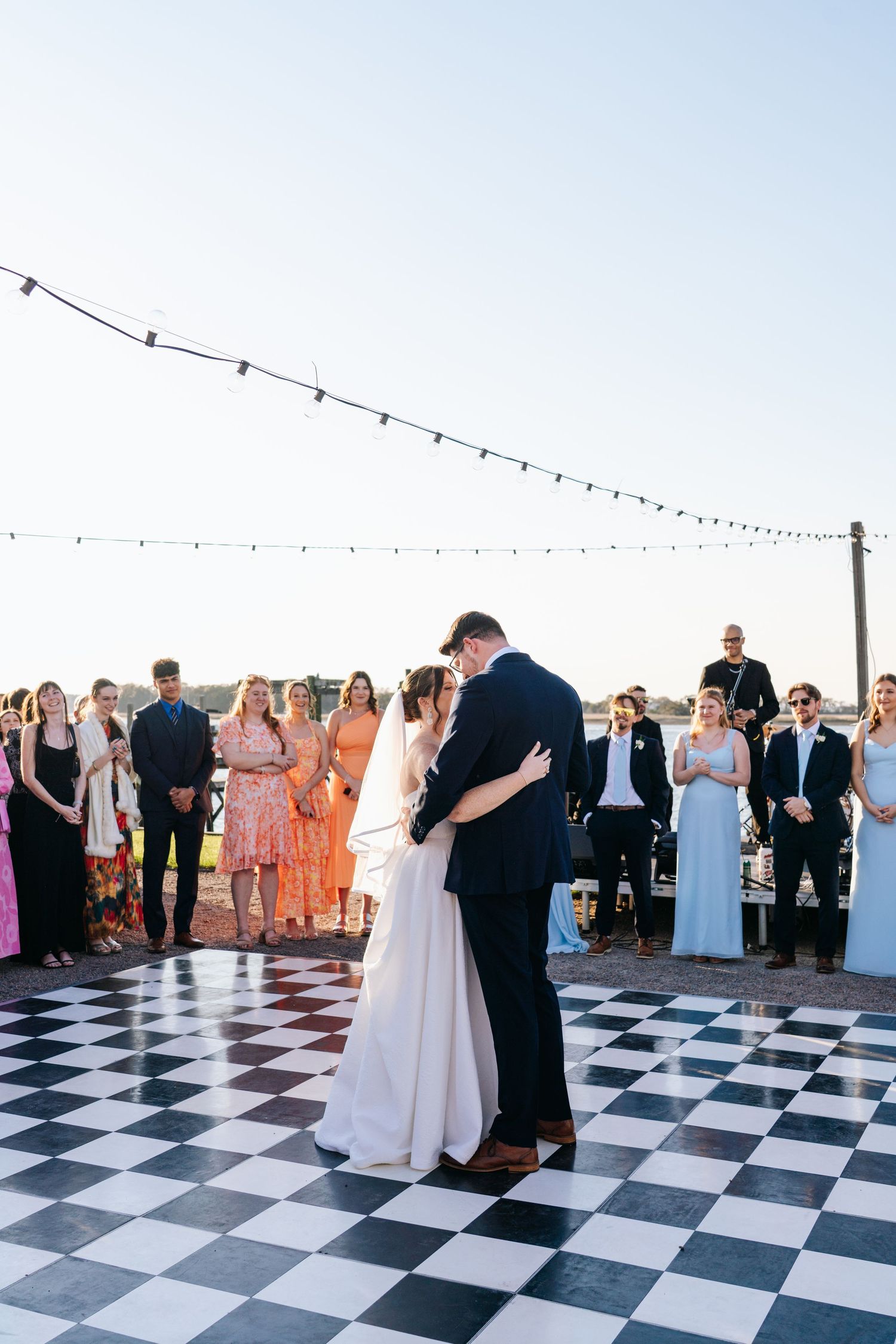 Couples dancing on a black and white checkered dance floor under string lights at an outdoor reception.