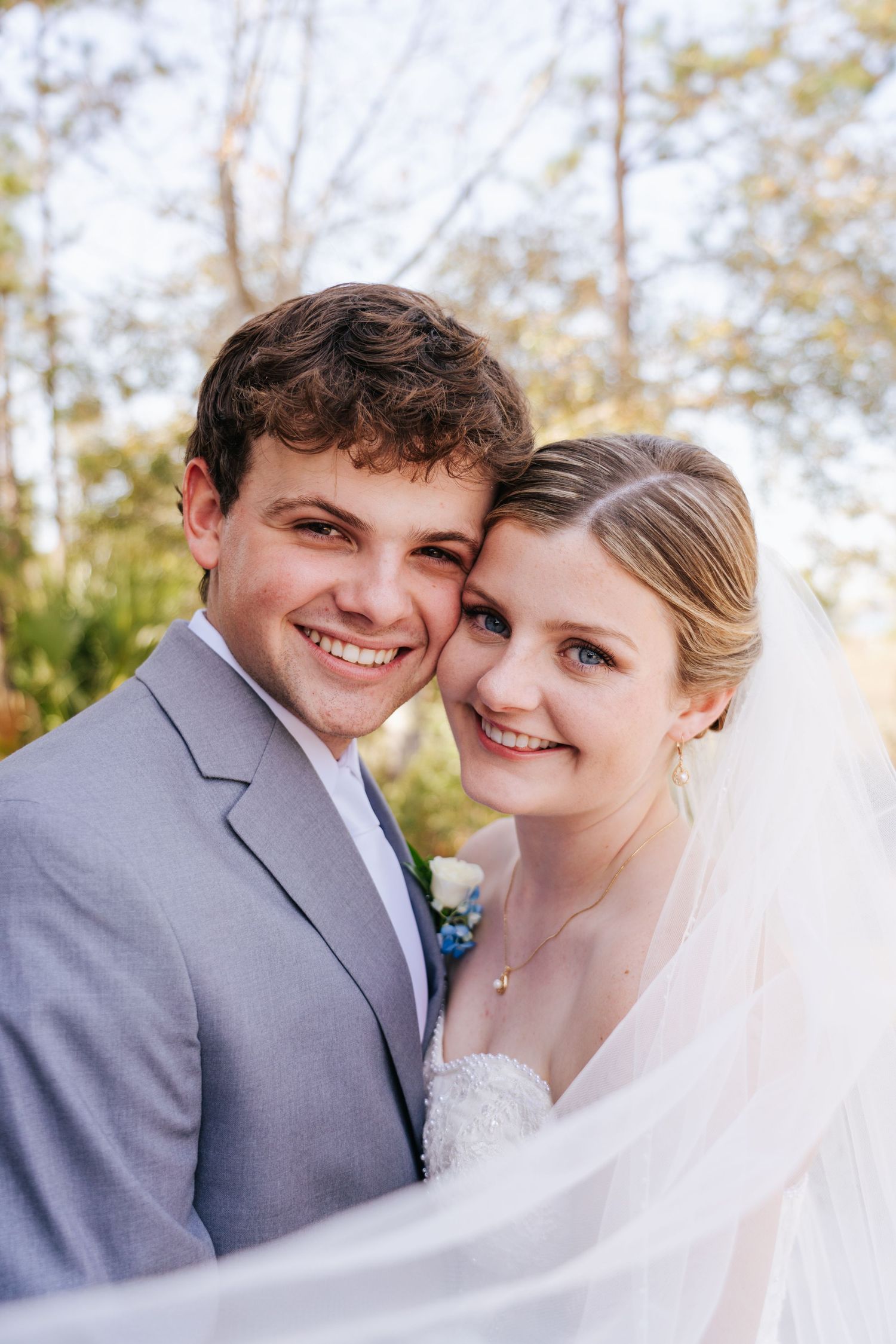 Couple in wedding attire sharing joyful moments against a natural backdrop.