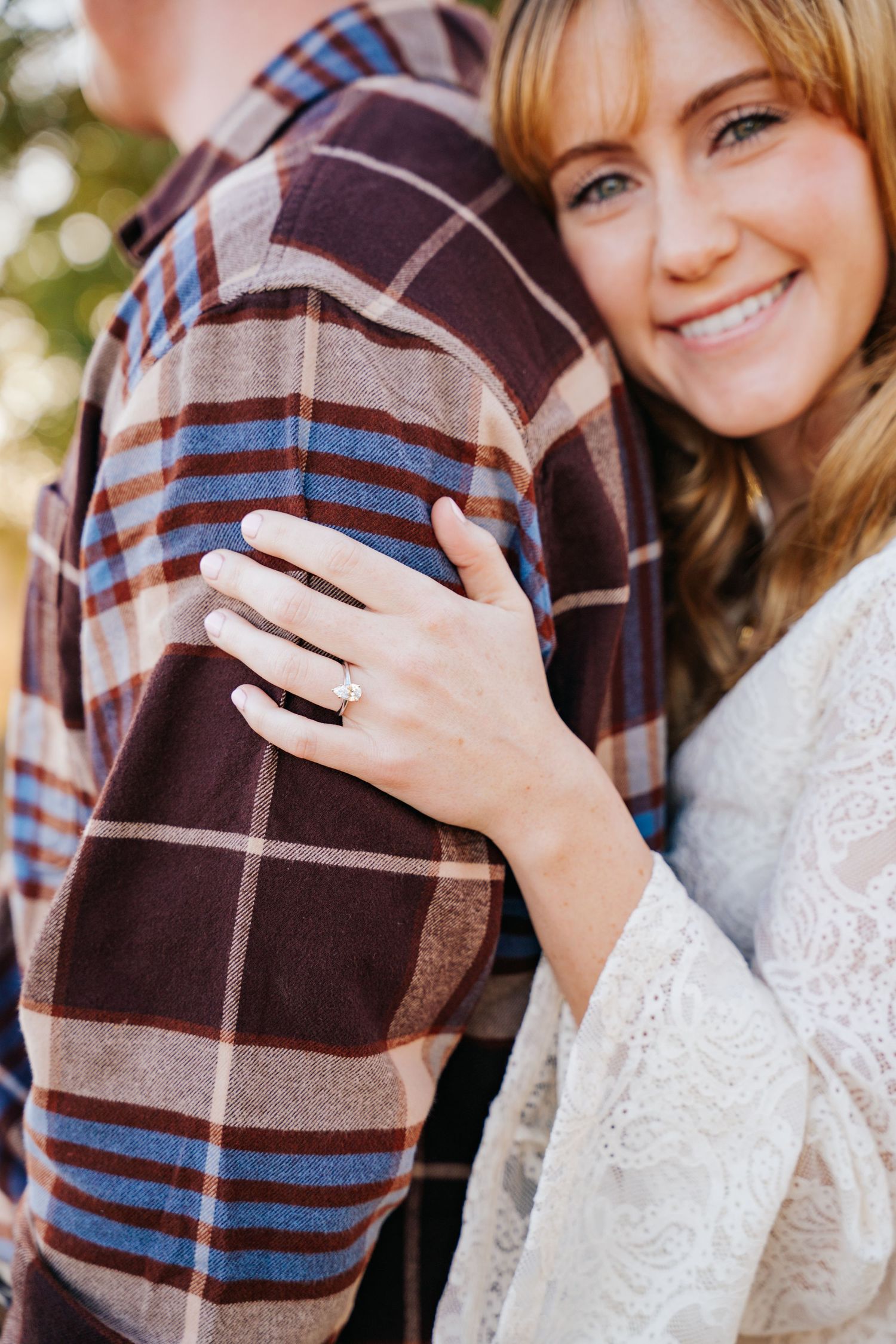 Close-up engagement ring photos showing couple embracing in plaid and white lace clothing during autumn photoshoot.