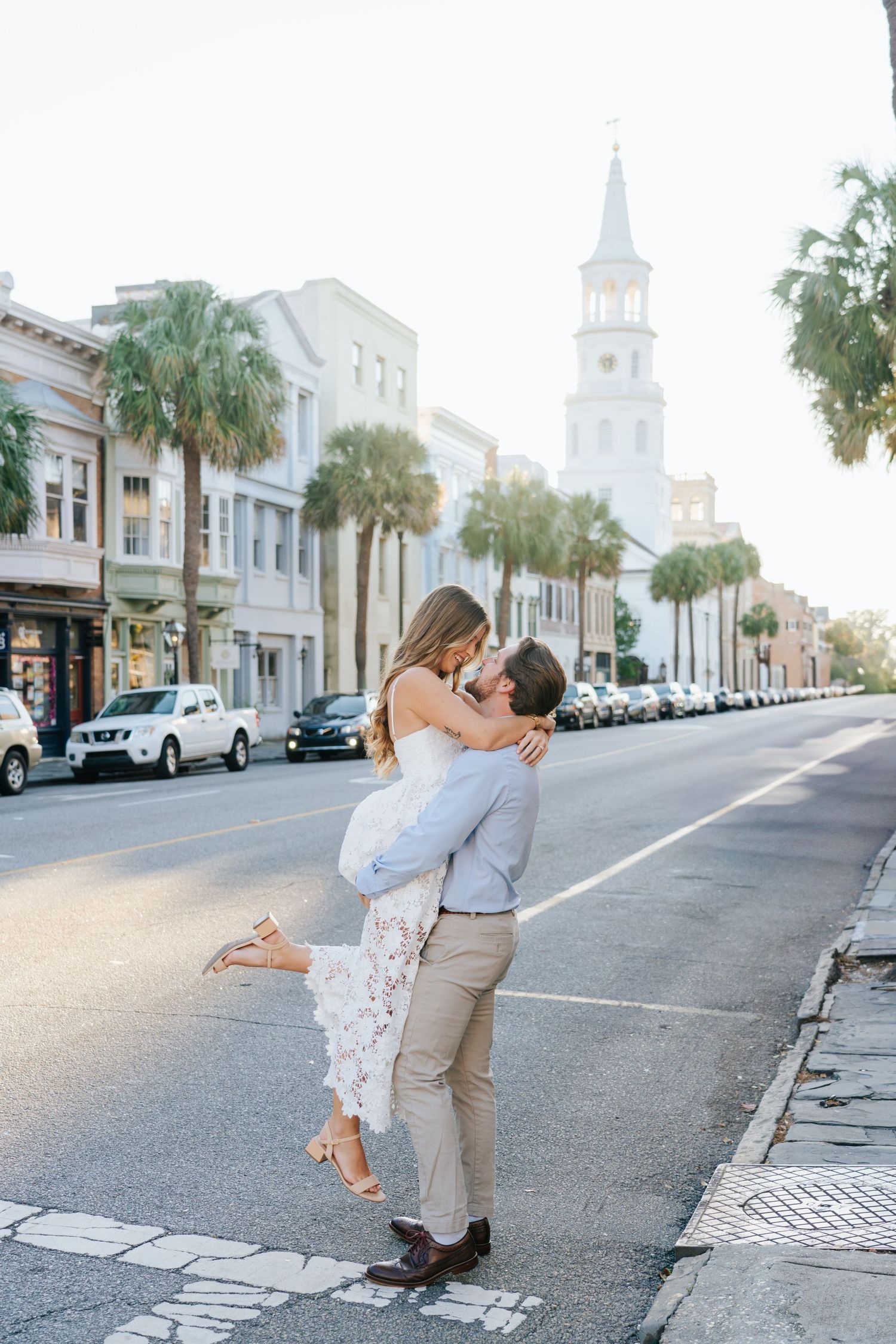 Romantic engagement photos on a historic Charleston street with palm trees and white buildings.