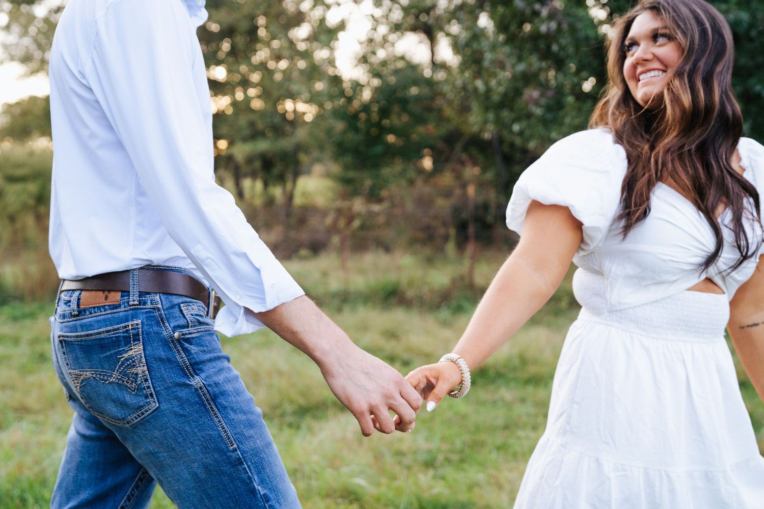 A group wearing white tops and blue jeans poses casually in a grassy outdoor setting during golden hour.