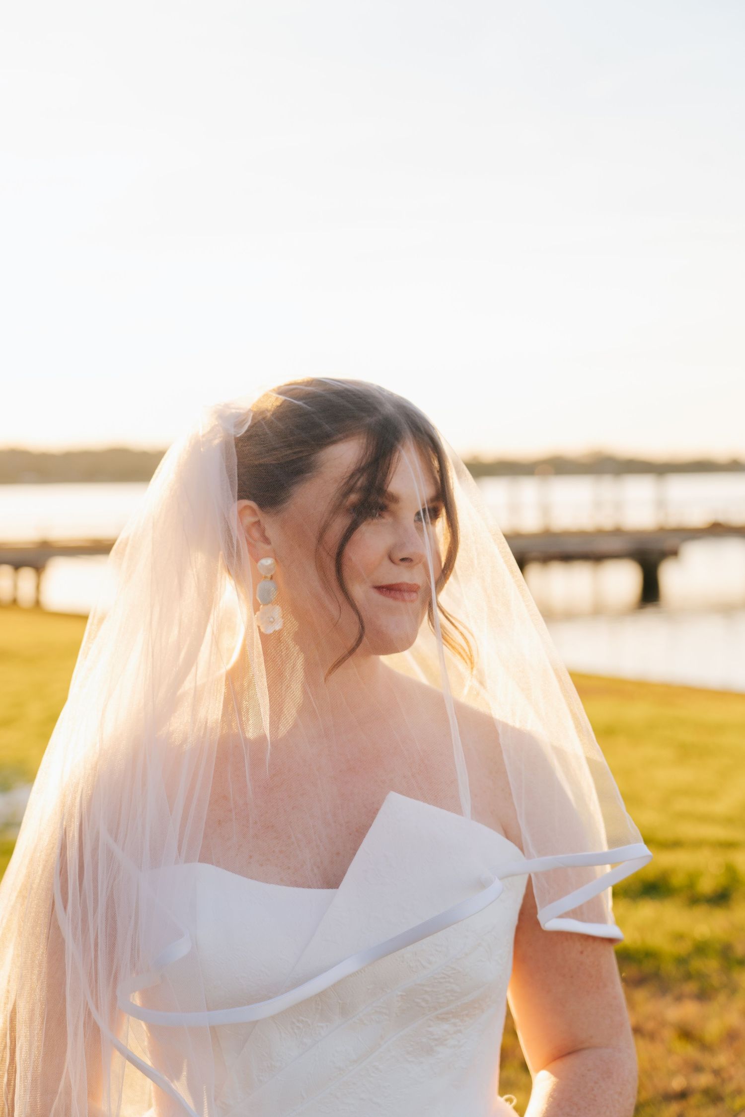 A delicate bridal veil flows in the breeze during a sunset photoshoot by the water.
