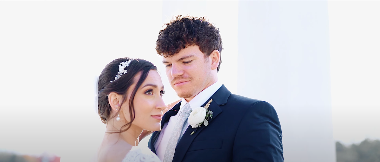 Couple shares an intimate moment during their wedding ceremony against a bright outdoor backdrop.