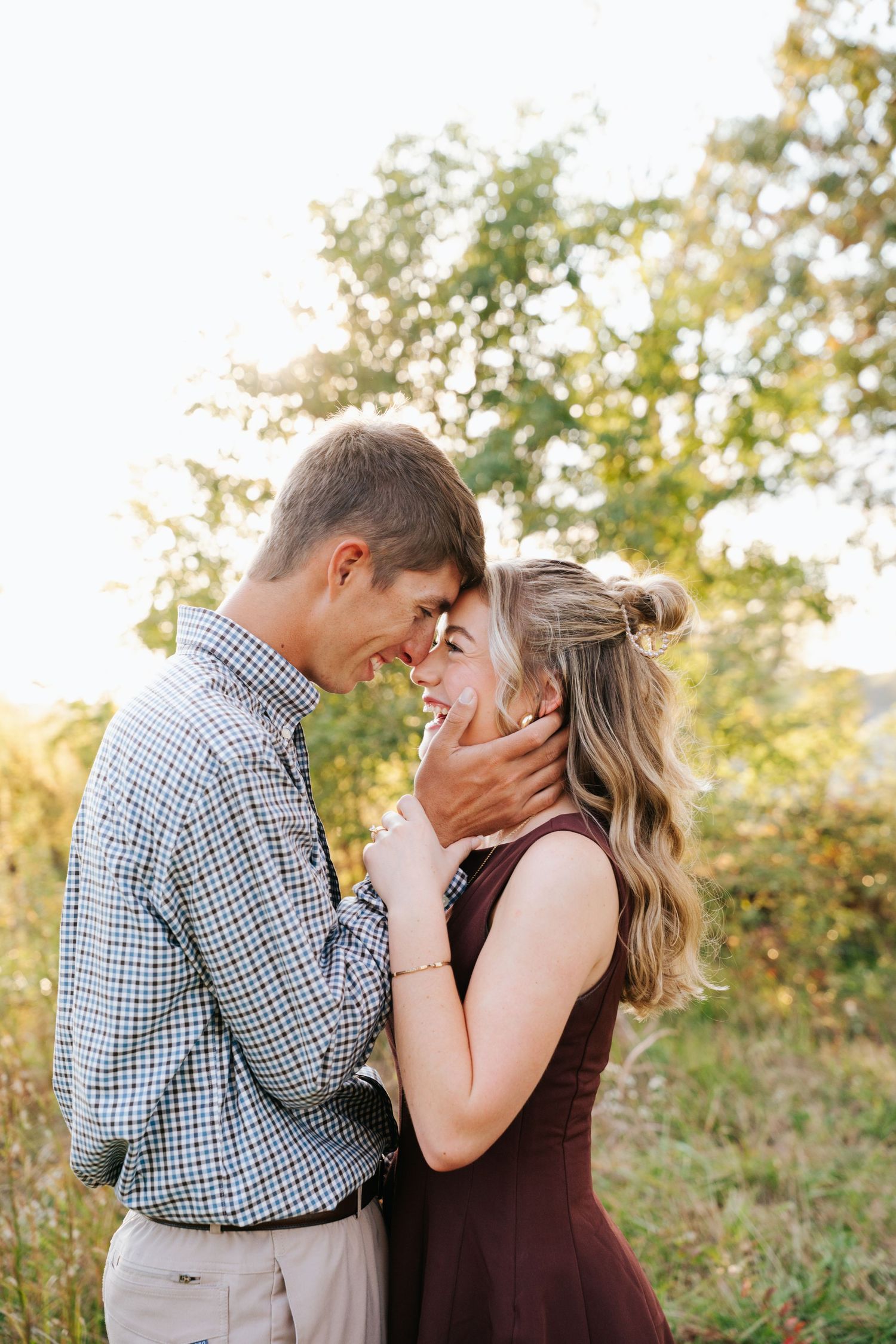 A romantic couple embraces outdoors during a sunset photo session in a natural setting.
