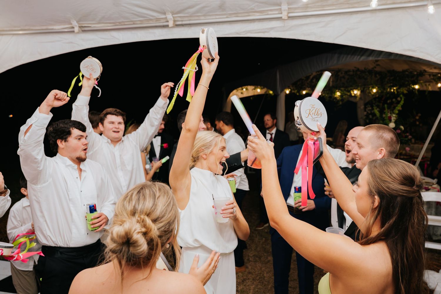 Wedding guests dance and celebrate together under a tent during an outdoor evening reception celebration.