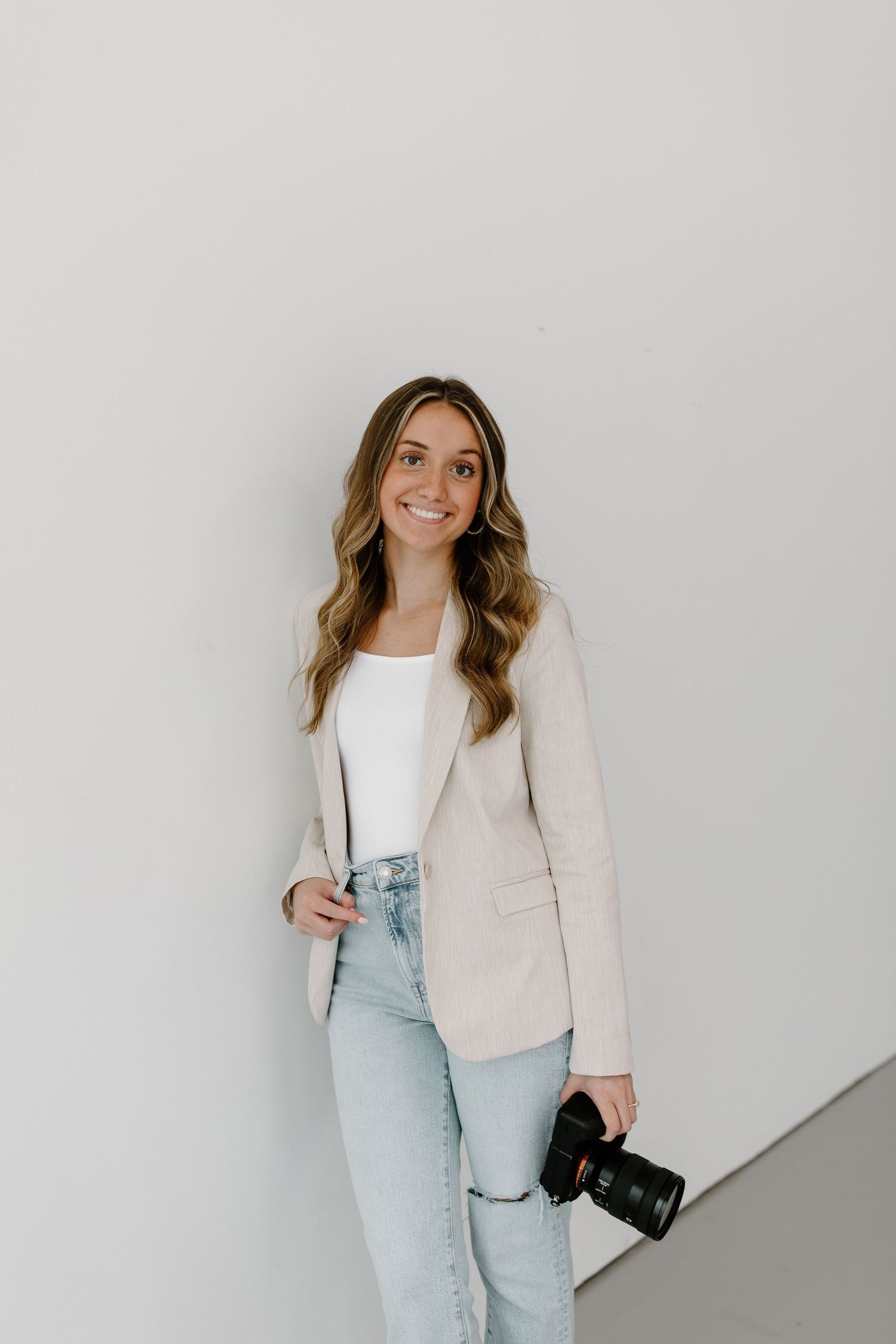 Portrait series of a photographer in light blazer and jeans holding camera against white background.