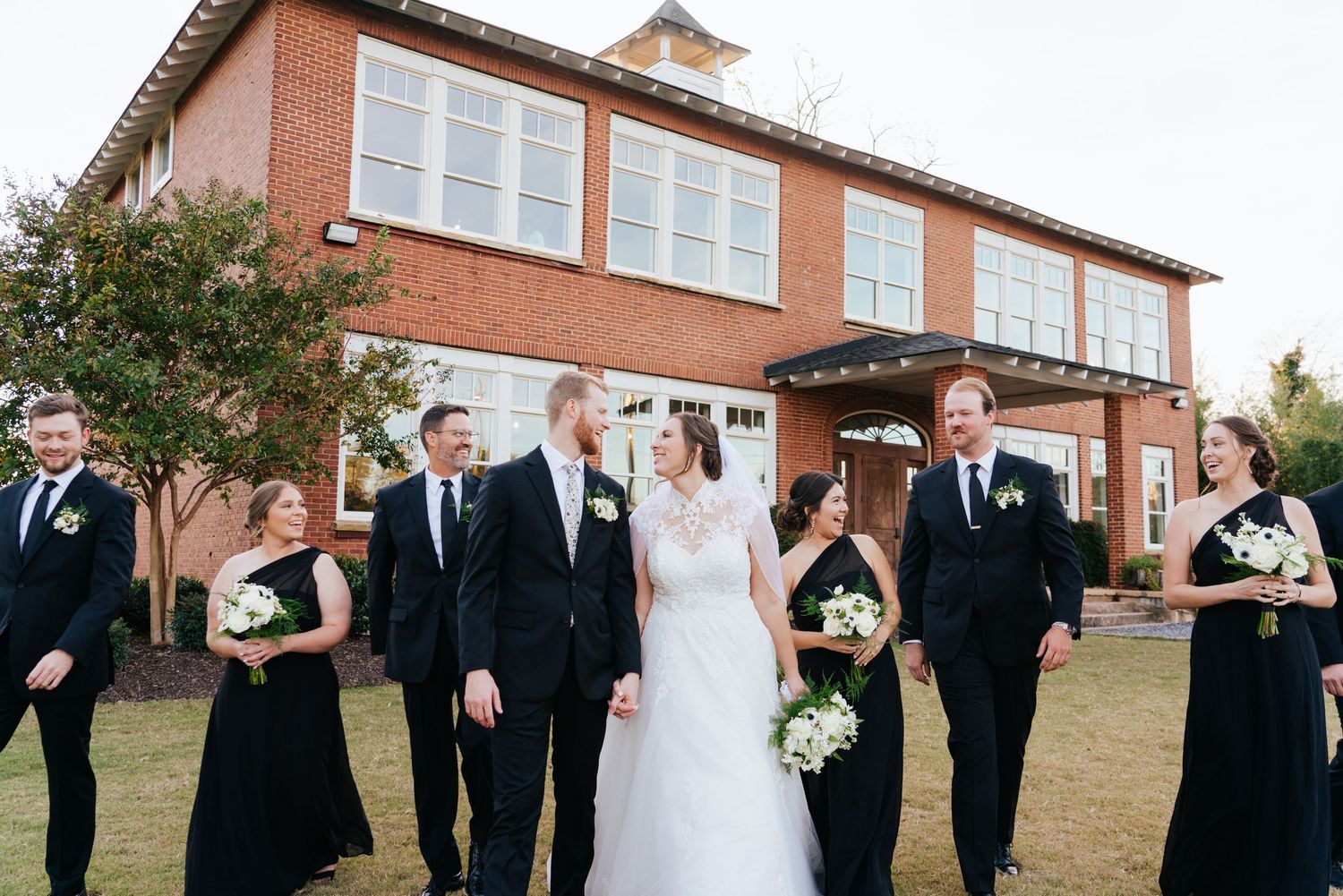 Wedding party poses in front of brick building during outdoor celebration.