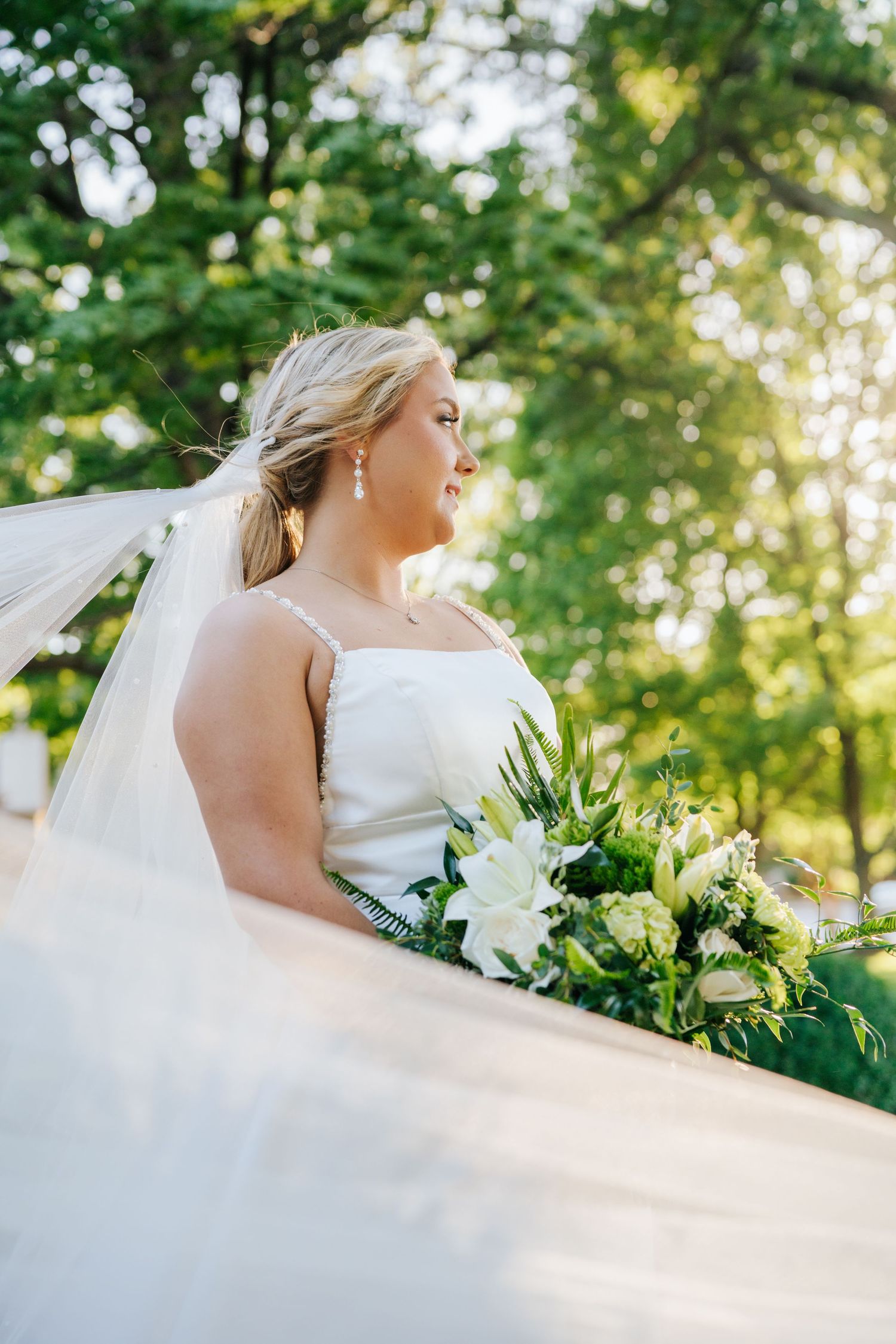 Ethereal bridal portrait with flowing veil and white bouquet in natural outdoor setting.