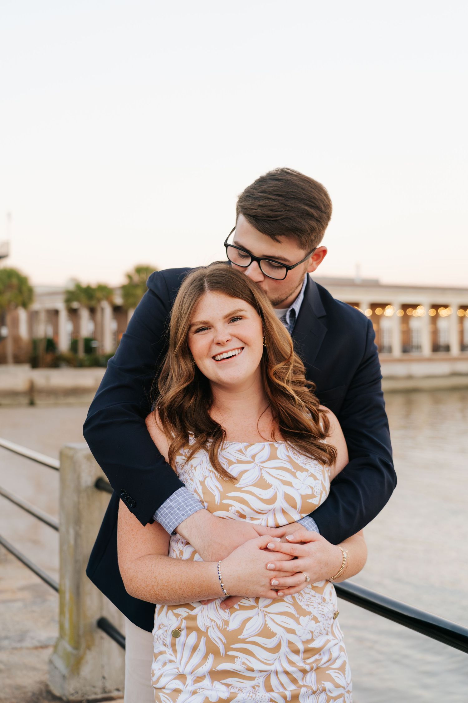 A couple embraces while standing near a waterfront during sunset.