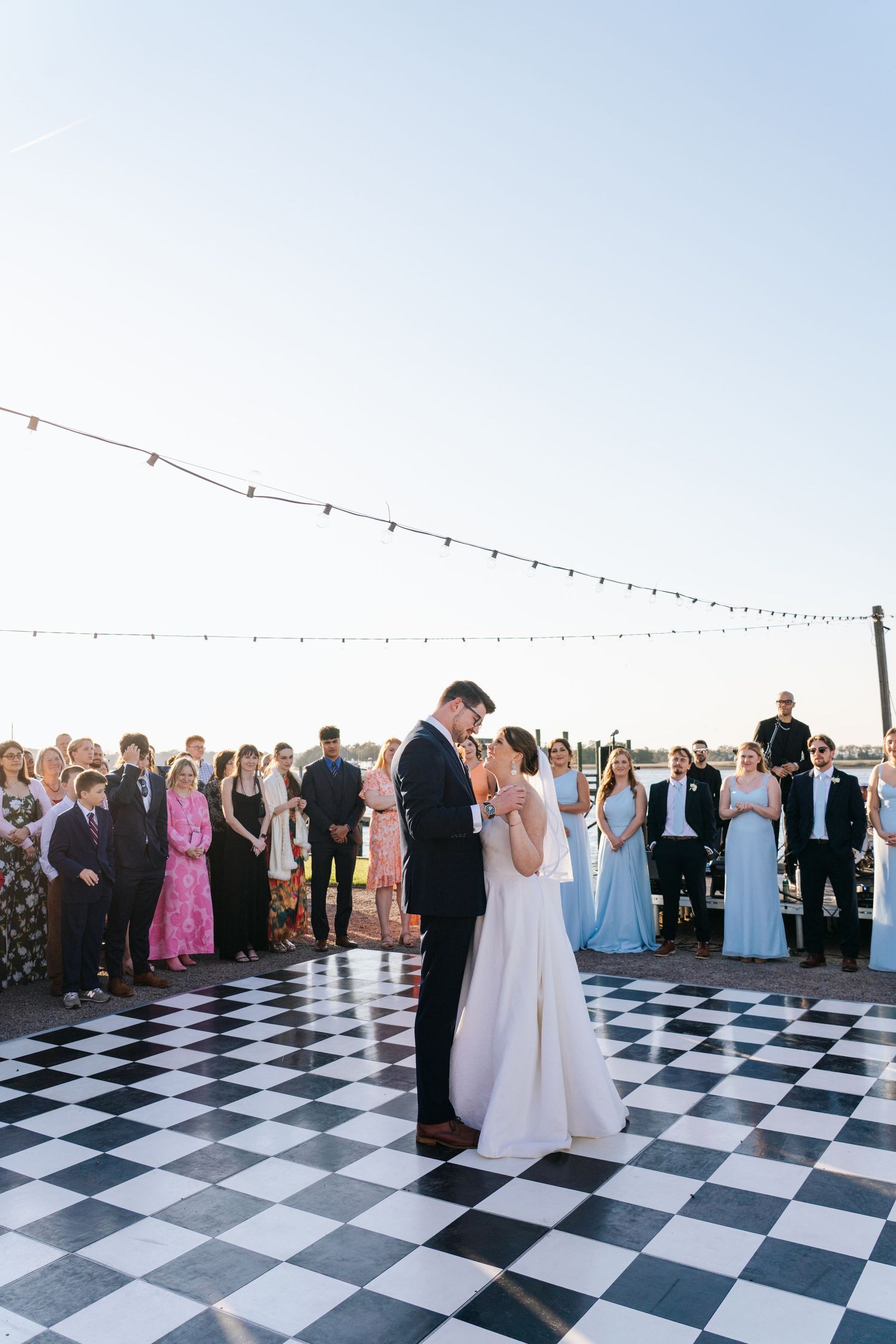 Wedding reception on a black and white checkered dance floor with string lights overhead.