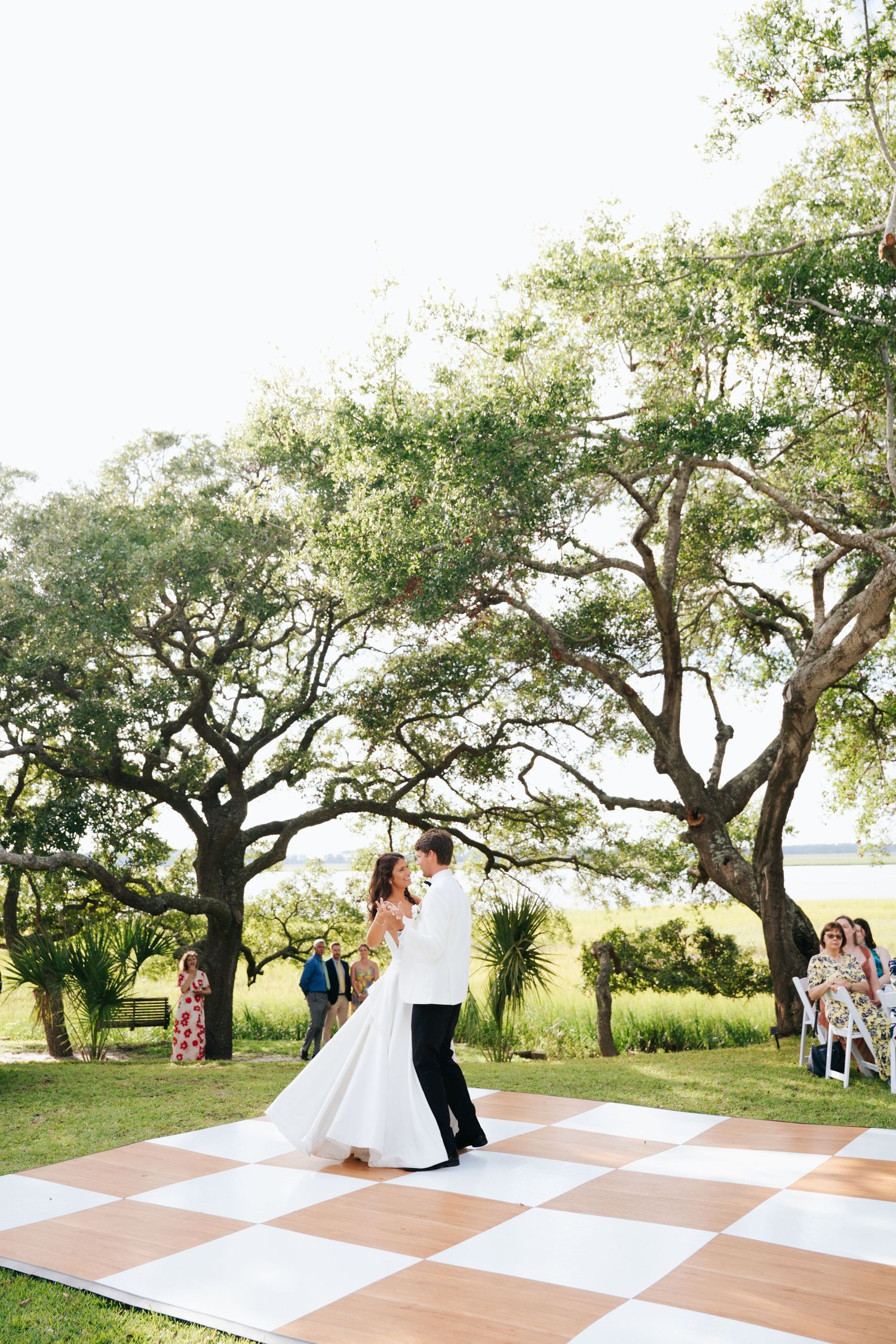 Couple sharing romantic dance on checkerboard dance floor with guests watching in background.