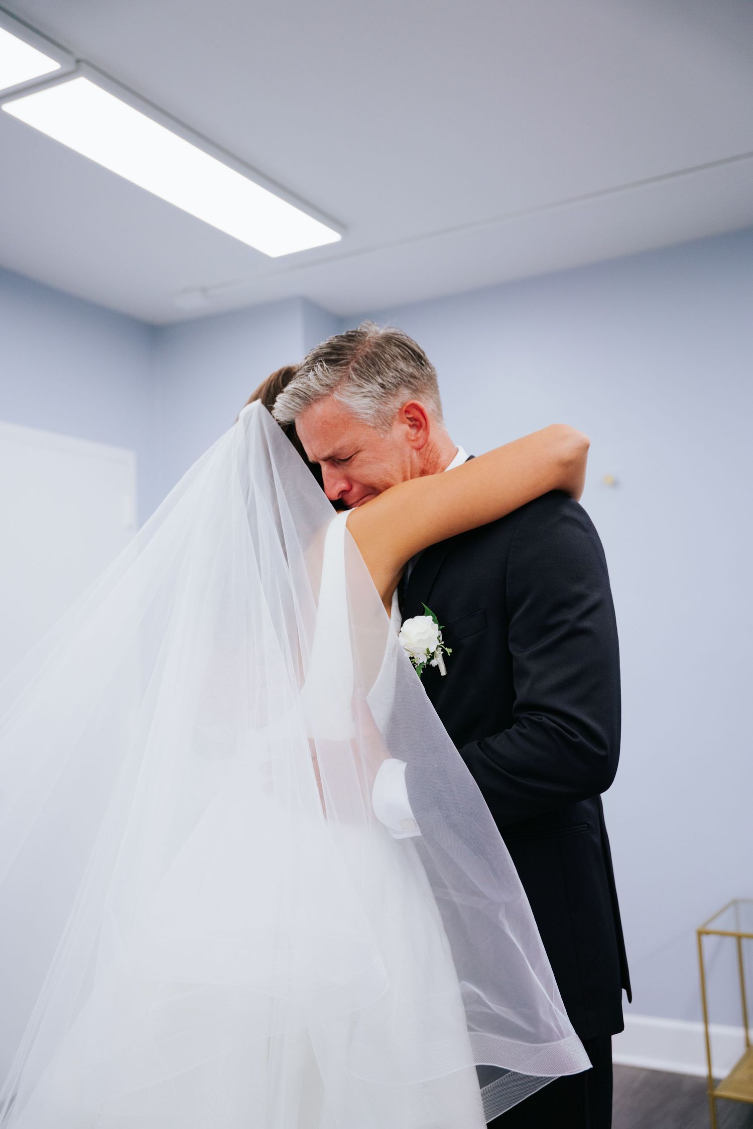 An intimate first look moment between bride and father, one in a white wedding dress and one in a black suit.