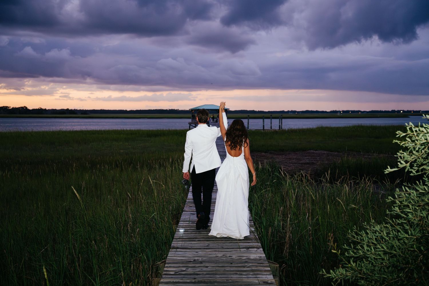 Couple walking along wooden boardwalk at dusk with stormy sky backdrop.