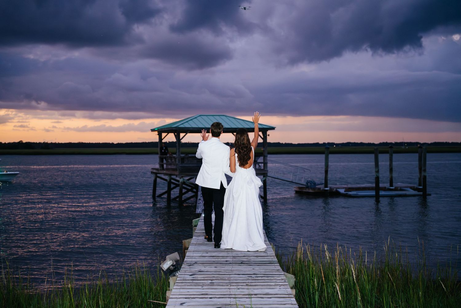 Dramatic sunset wedding photos taken on a wooden pier over water with dark clouds in the background.