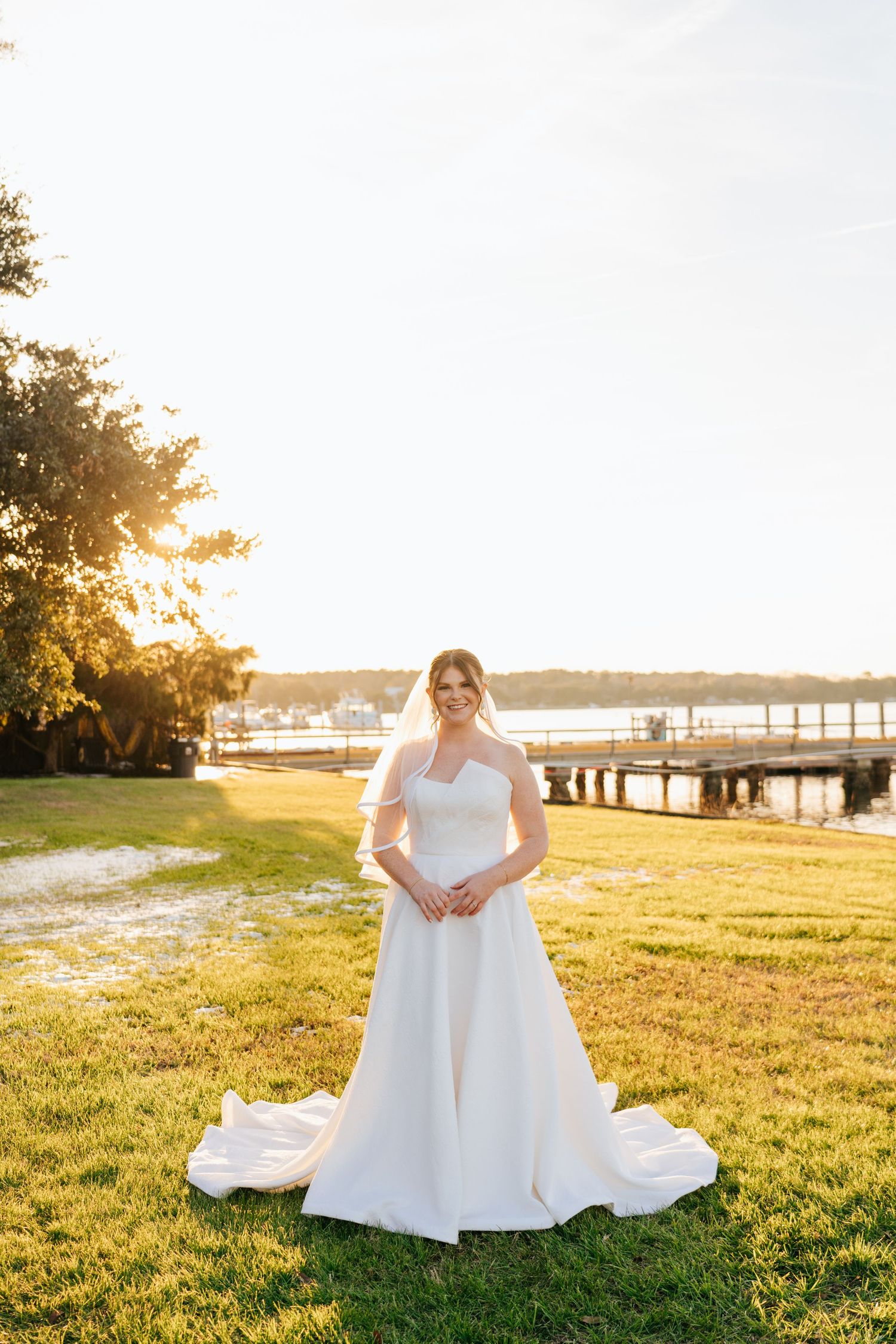A bridal portrait at sunset shows a flowing white dress against a waterfront backdrop.