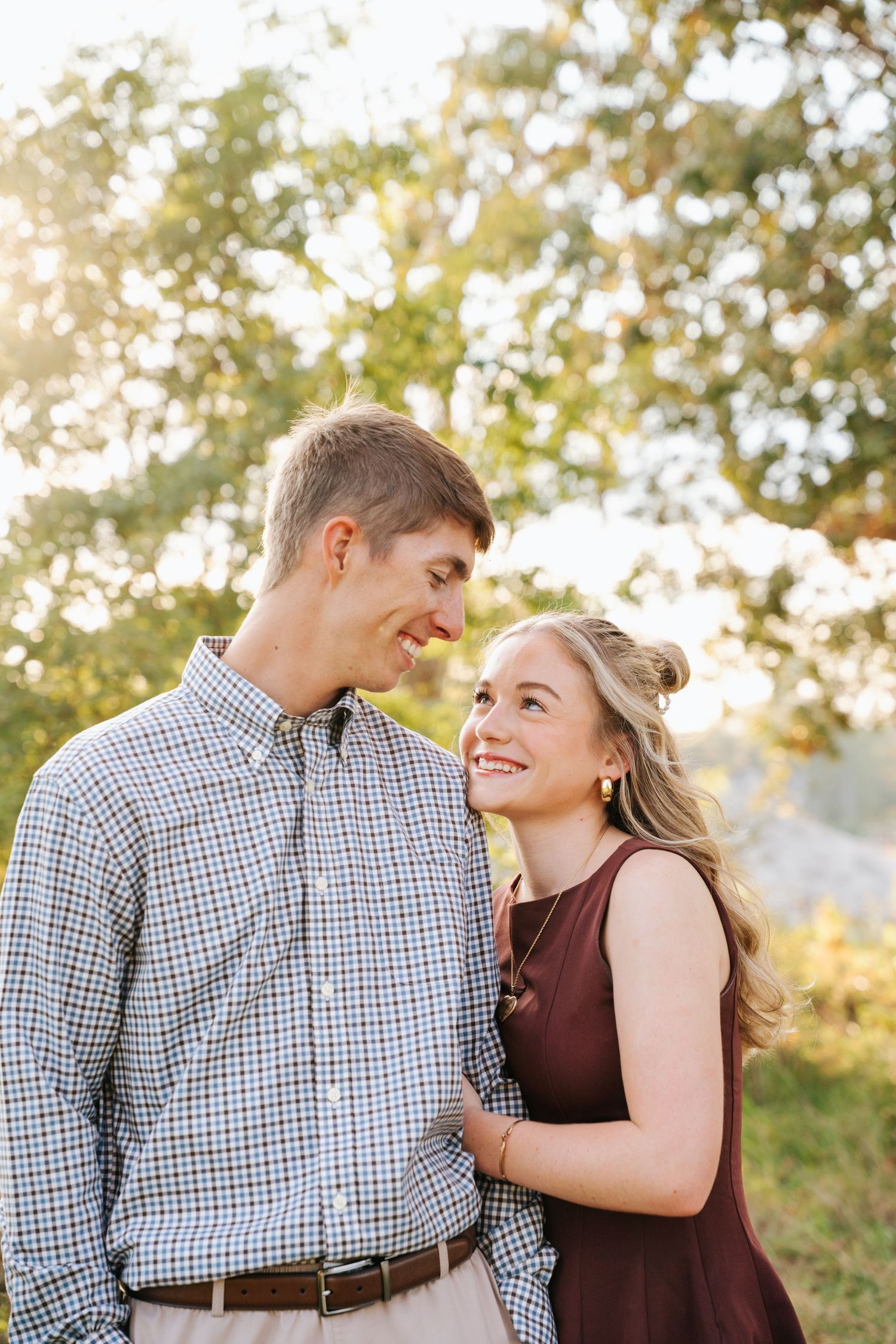 A couple shares joyful laughter together during an outdoor photoshoot in warm sunlight.